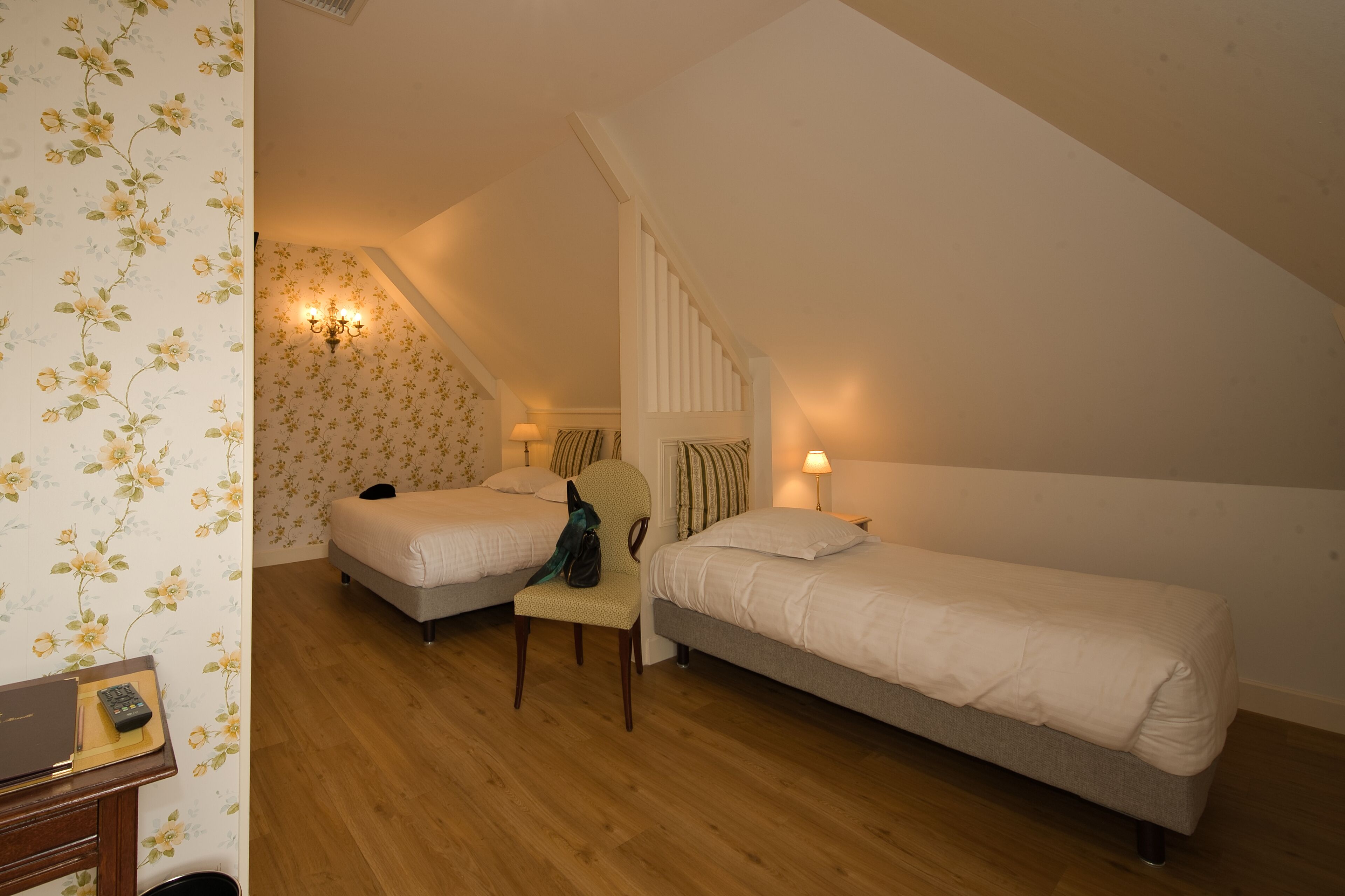 A bedroom with two single beds, a chair, a desk with a laptop, and a lamp.