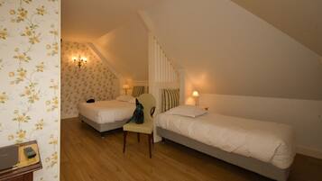 A bedroom with two single beds, a chair, a desk with a laptop, and a lamp.