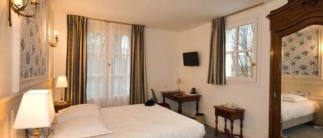 Habitación de hotel con una cama grande, una mesita de noche con lámpara, una pequeña mesa con lámpara, un televisor en la pared y un espejo.