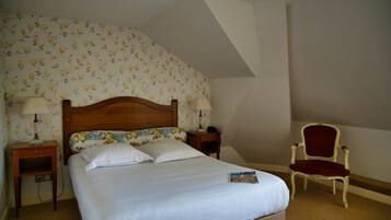 A neatly made bed with white linens, two bedside tables with lamps, a floral-patterned headboard, and a red upholstered chair.