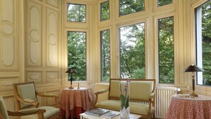 Una habitación con ventanas amplias, una mesa con un libro, un florero con flores y dos sillas.