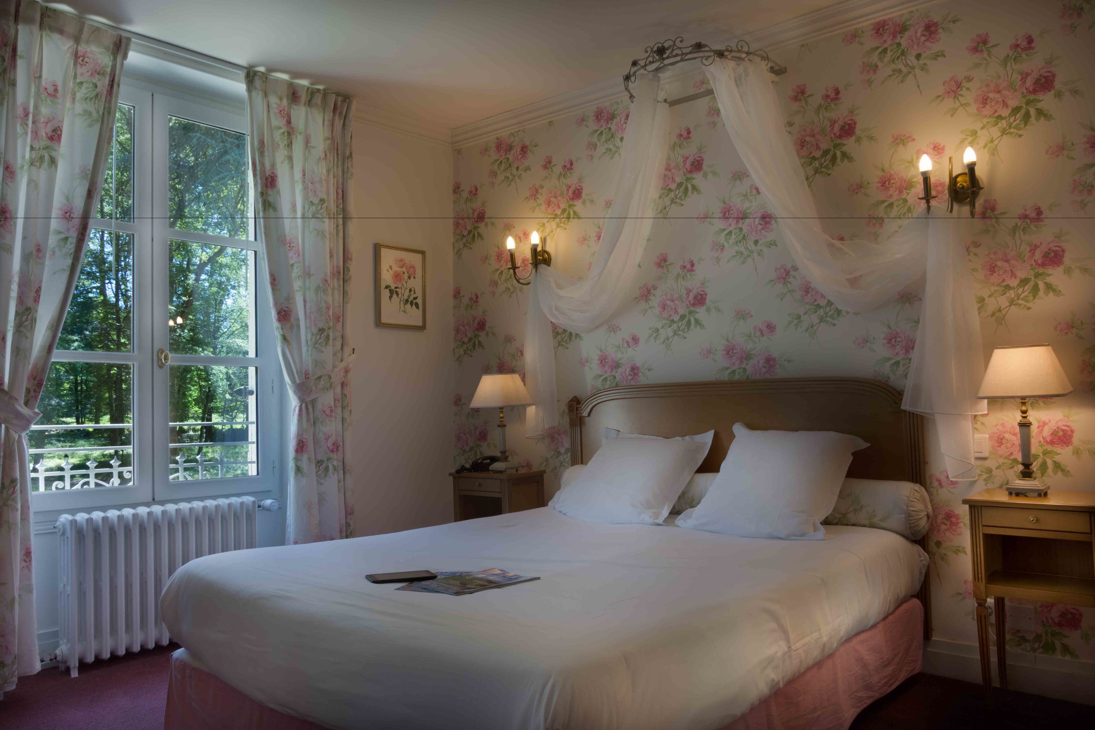 A neatly made bed with white linens, a bedside table with a lamp, and a window with curtains.