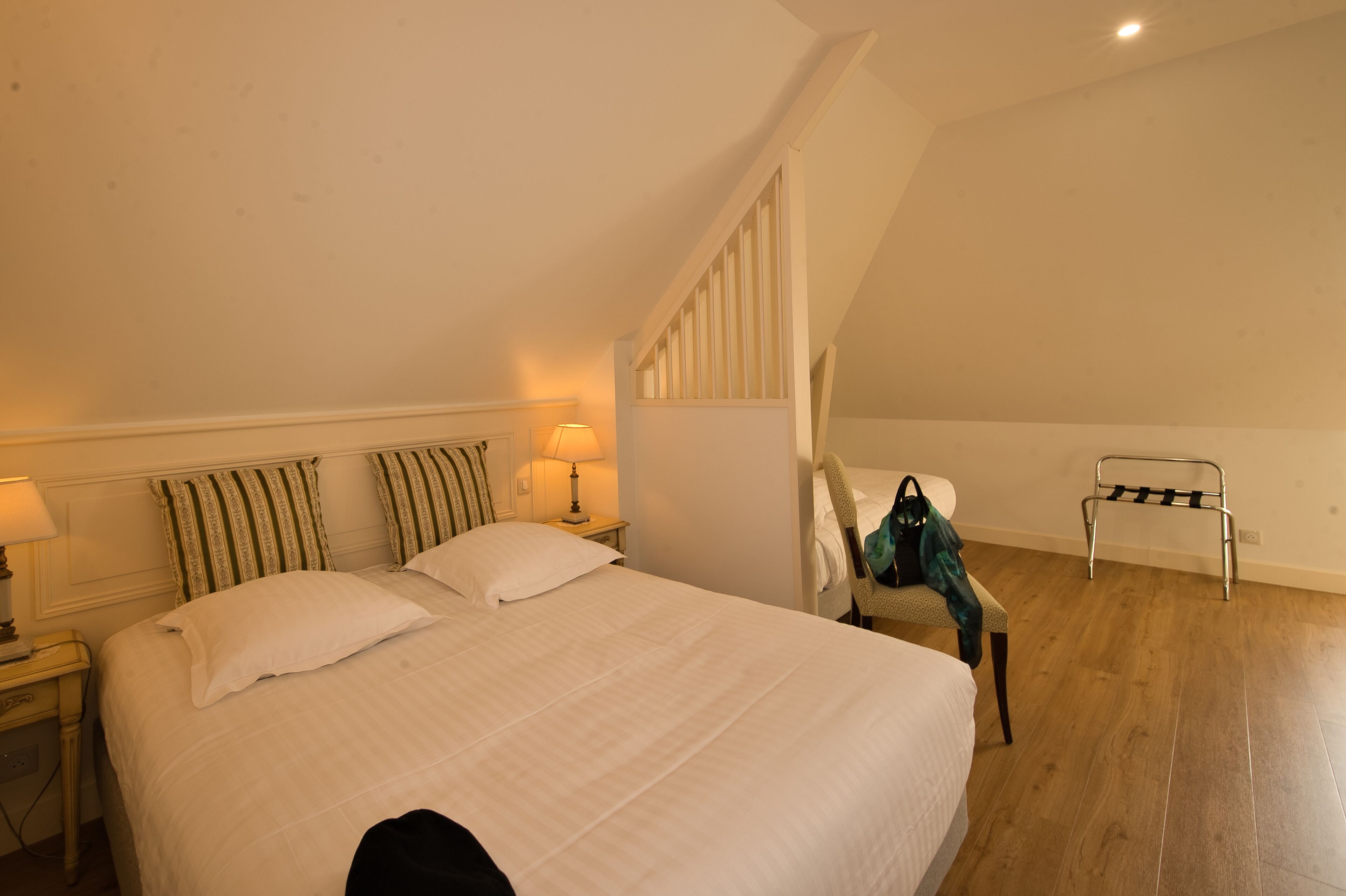 A bedroom with a large bed, a nightstand with a lamp, a chair, and a luggage rack.