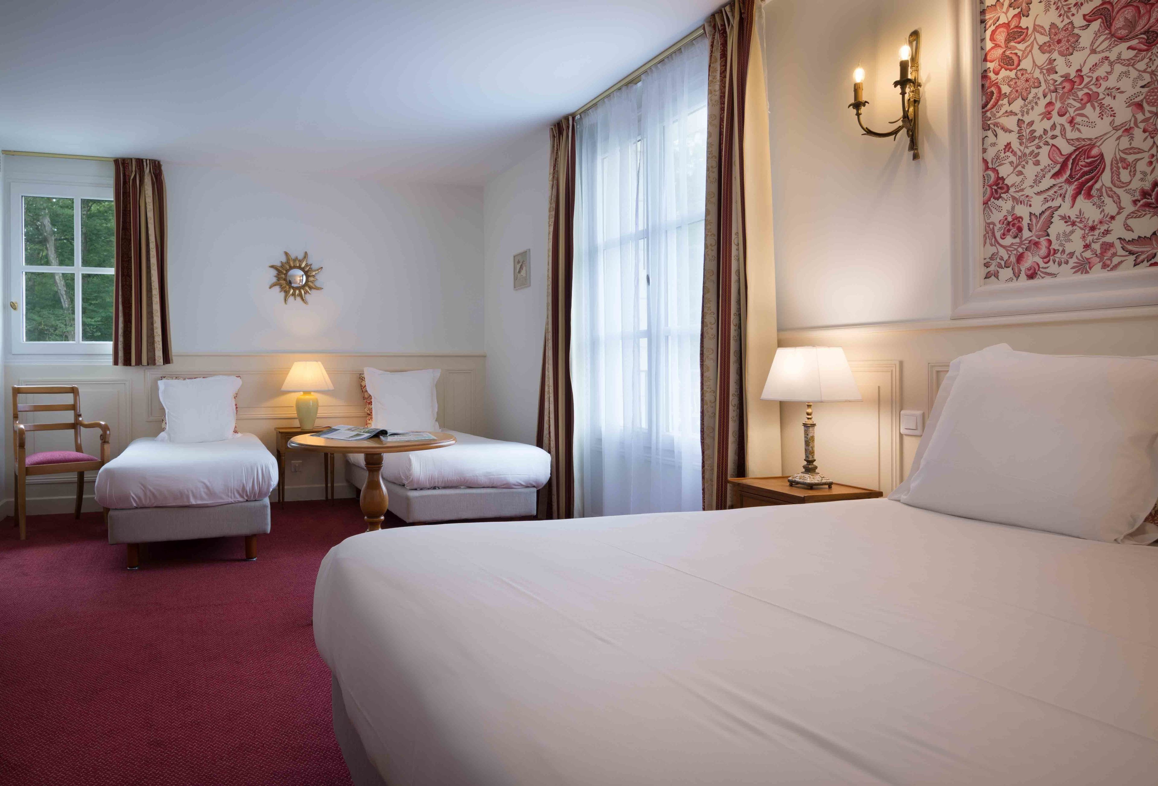 A hotel room with a large bed, two bedside tables with lamps, a chair, a small table, and a decorative wall piece.