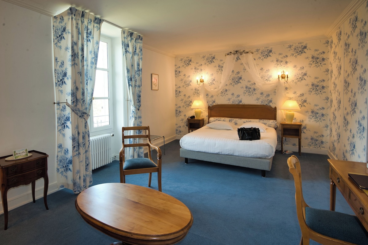 Une chambre à coucher comprenant un lit, deux tables de chevet, une chaise, une table en bois et une fenêtre avec des rideaux.
