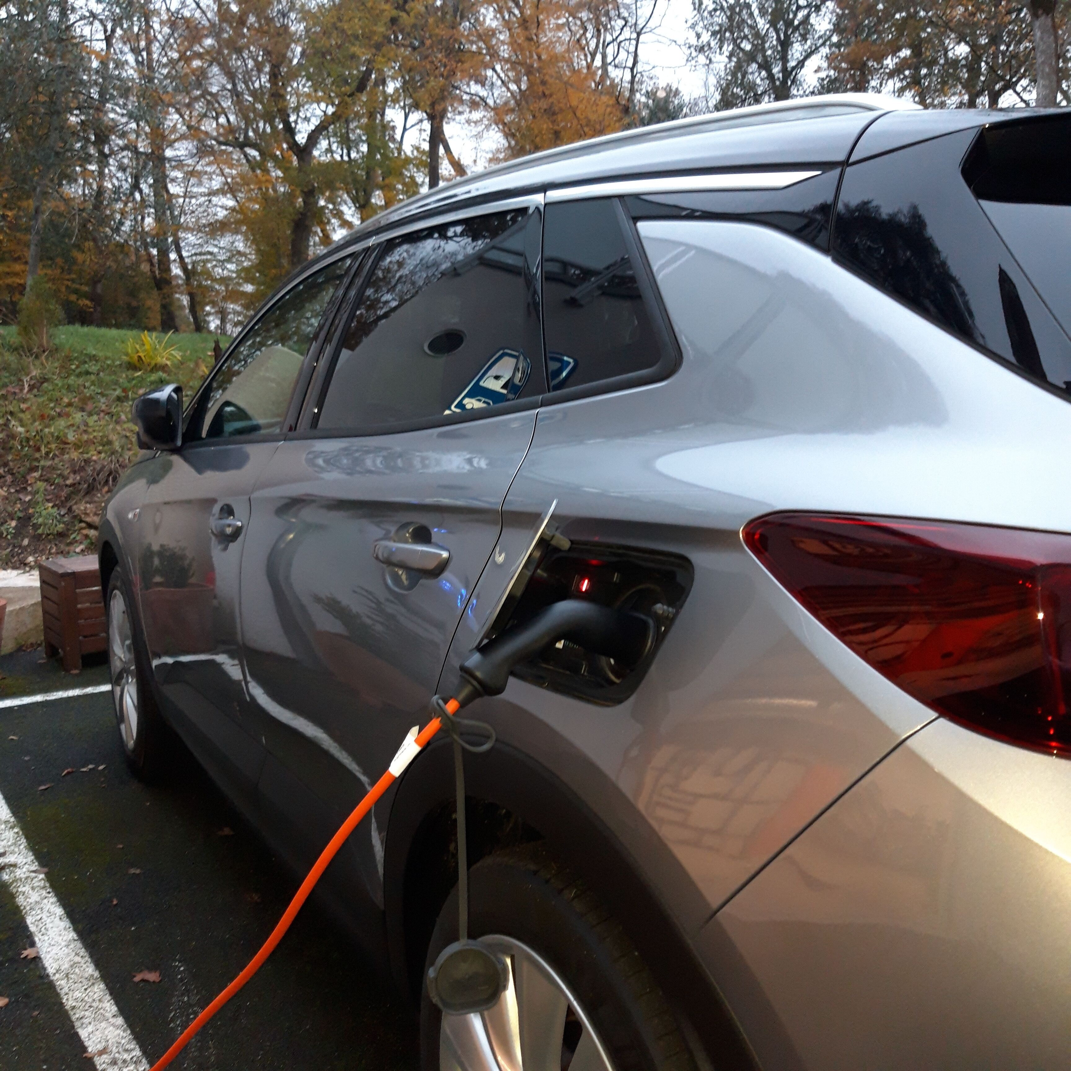 A silver SUV parked in a parking lot with a charging cable connected to the rear.