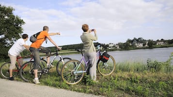 A group of people with bicycles near a body of water, possibly a lake, with houses in the background.