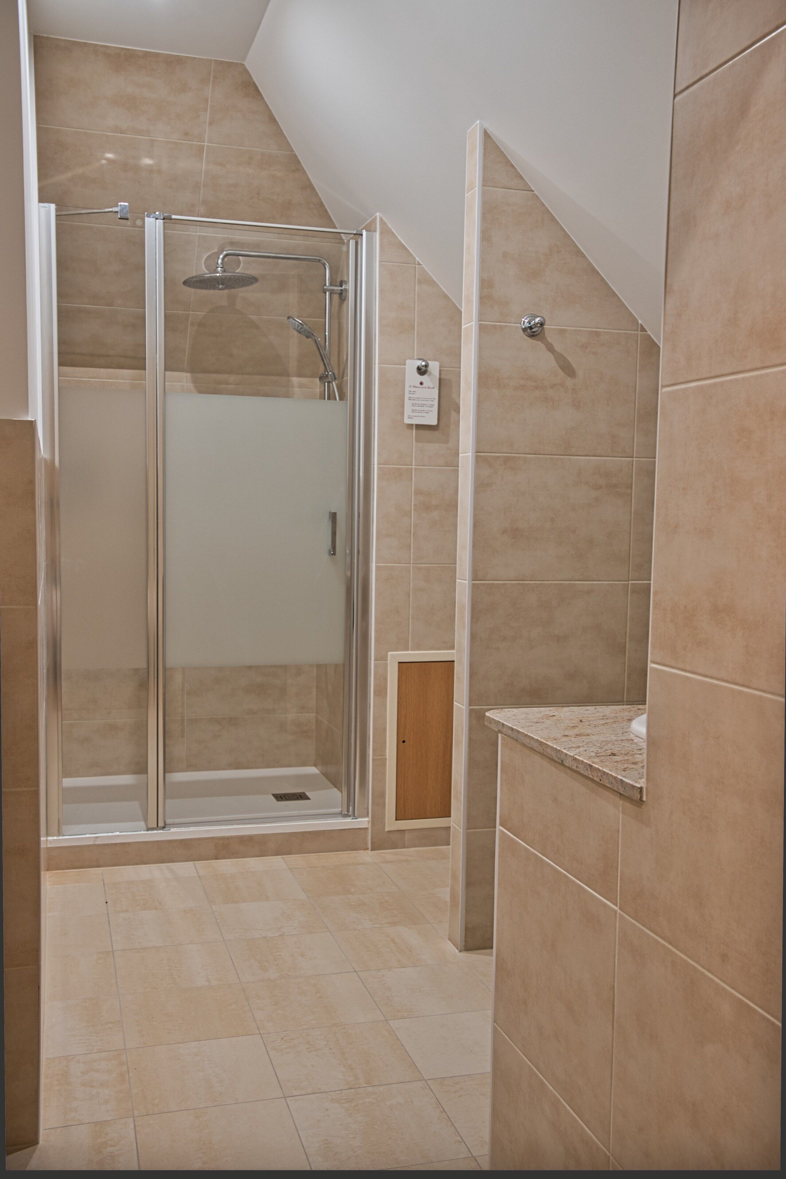 A glass-enclosed shower with a handheld showerhead and a wall-mounted faucet.