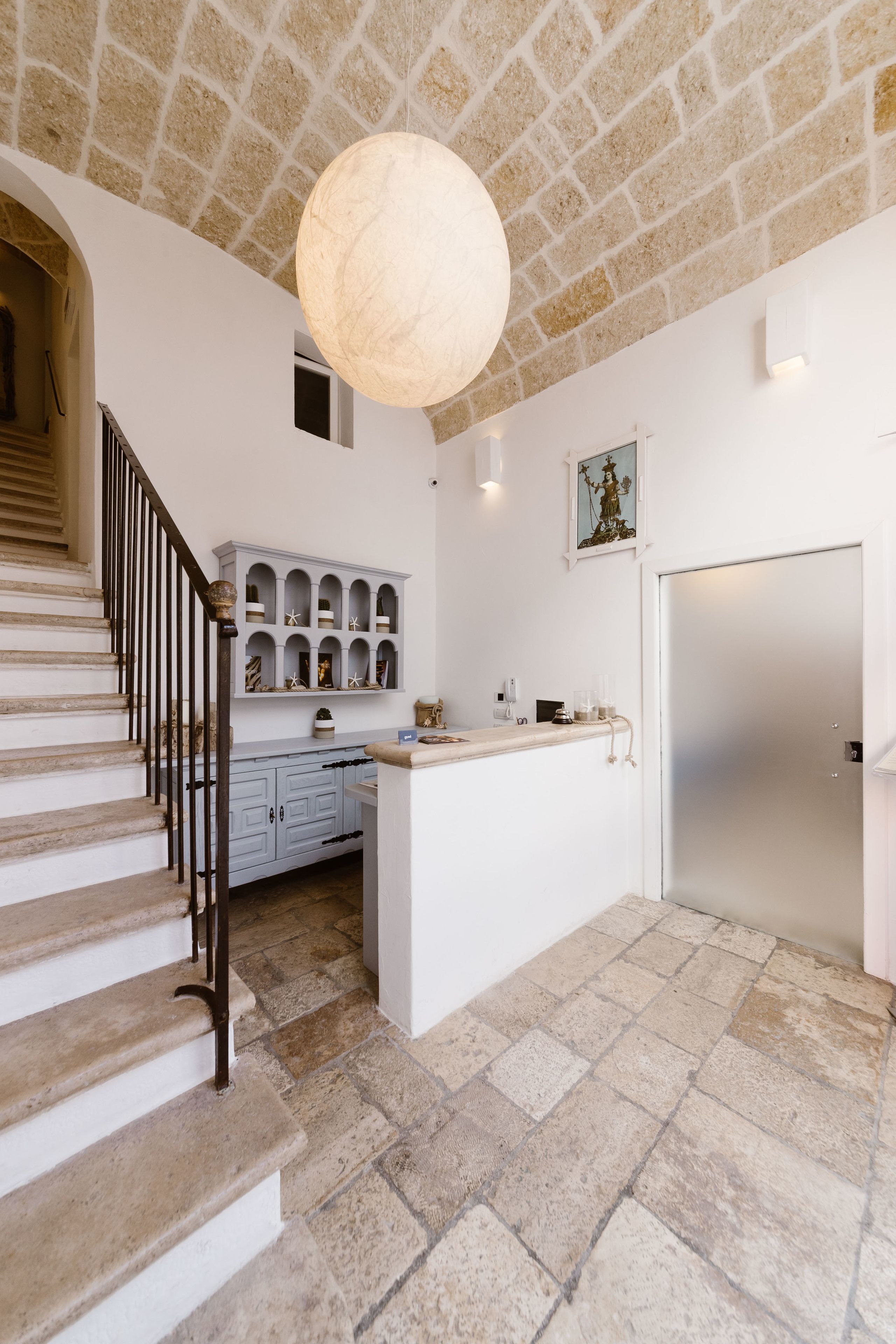 A staircase with stone steps and a metal railing, leading to a white kitchen area with a marble countertop and built-in shelving.