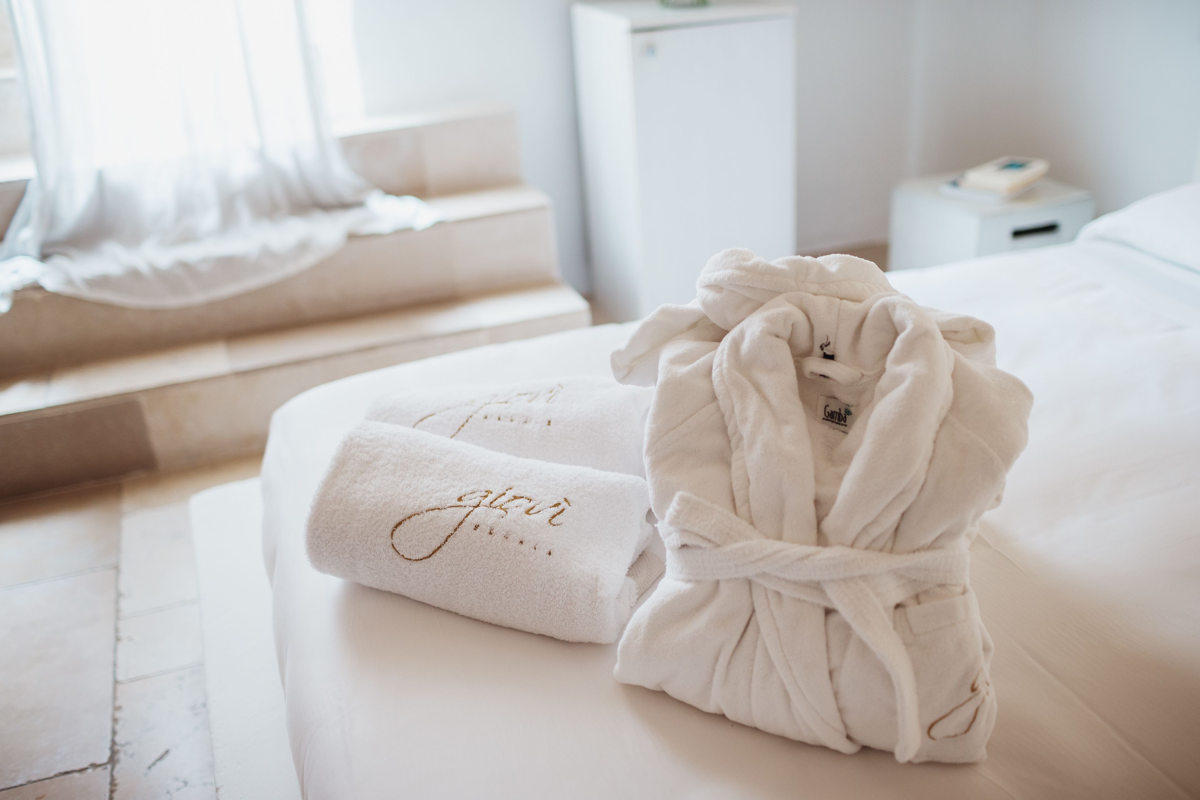 Una cama bien hecha con un albornoz blanco y una toalla con texto bordado.