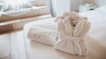 Una cama bien hecha con un albornoz blanco y una toalla con texto bordado.