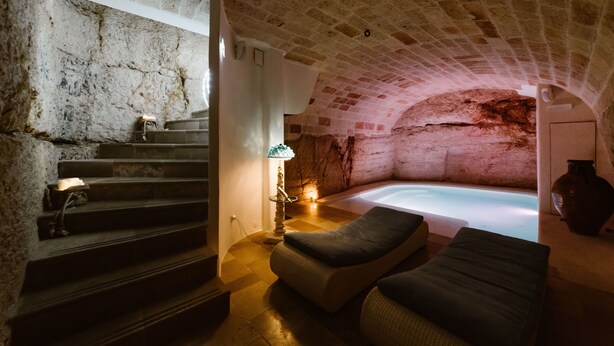A stone-walled room with a bathtub, a staircase, and a sofa.