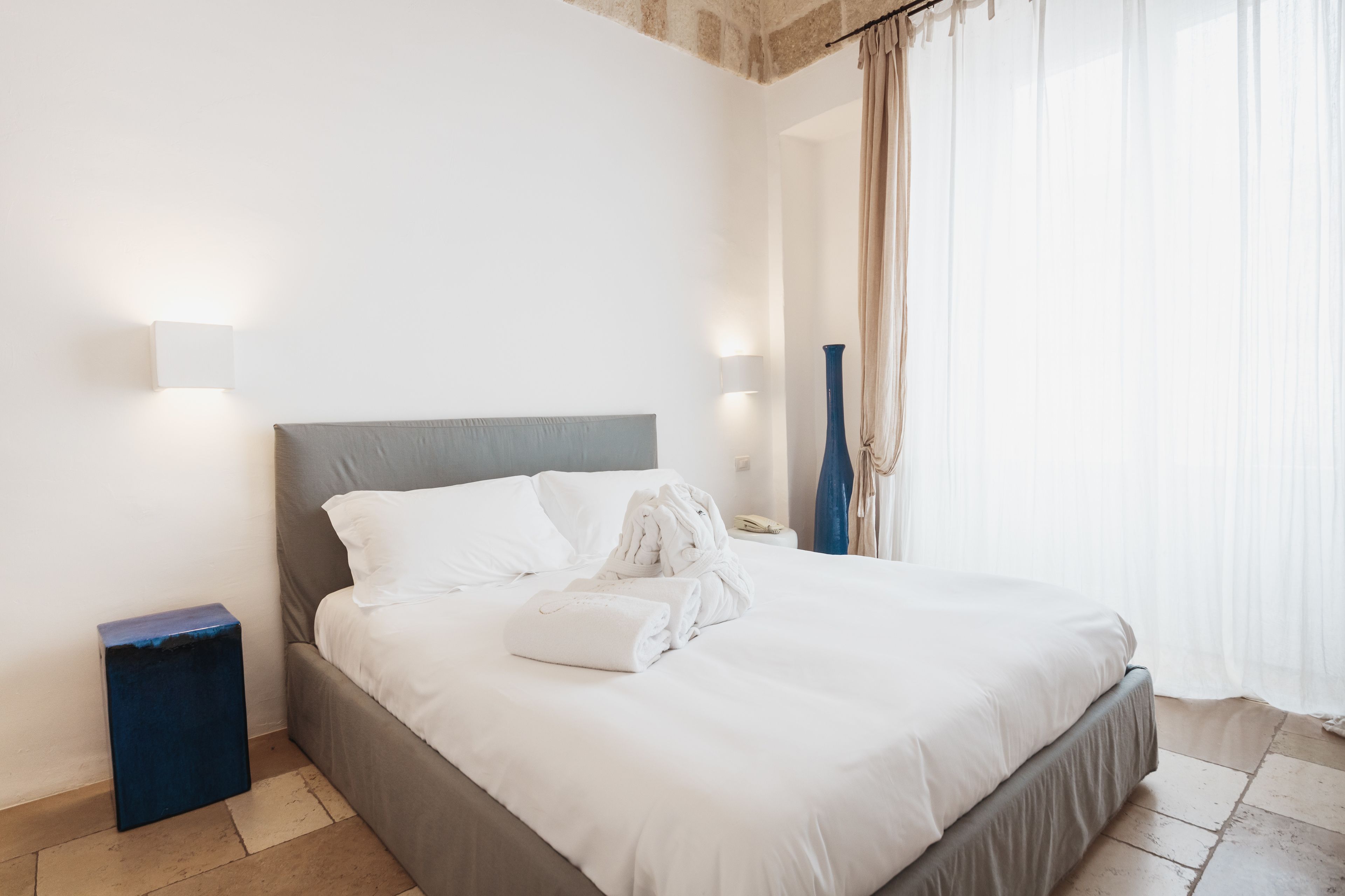 Una cama bien hecha con sábanas blancas y cabecera gris en una habitación de hotel.