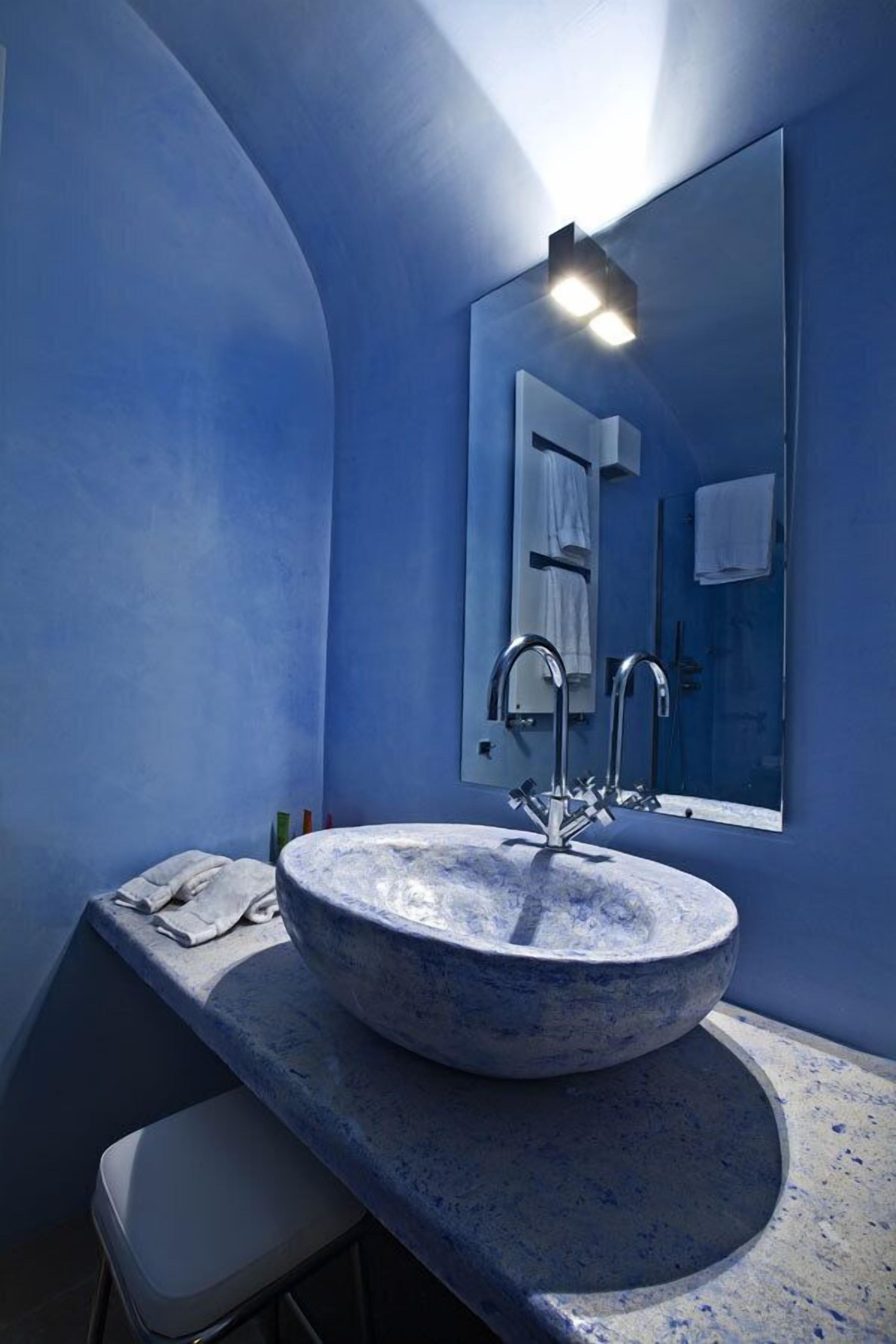 A bathroom with a large round sink, a mirror, and a stool.