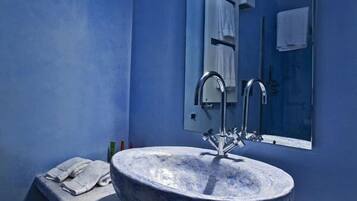 A bathroom with a large round sink, a mirror, and a stool.