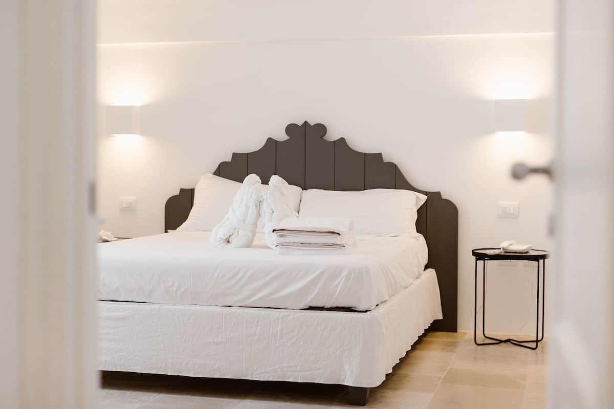 A neatly made bed with white linens, a dark headboard, and two bedside lamps.