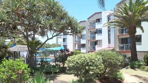 A resort with a pool, palm trees, and a building with balconies. - Casablanca Beachfront Holiday Apartments (Kings Beach)