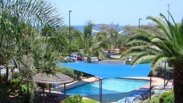 A pool area with a clear view of the ocean, surrounded by palm trees and a covered seating area. - Casablanca Beachfront Holiday Apartments (Kings Beach)