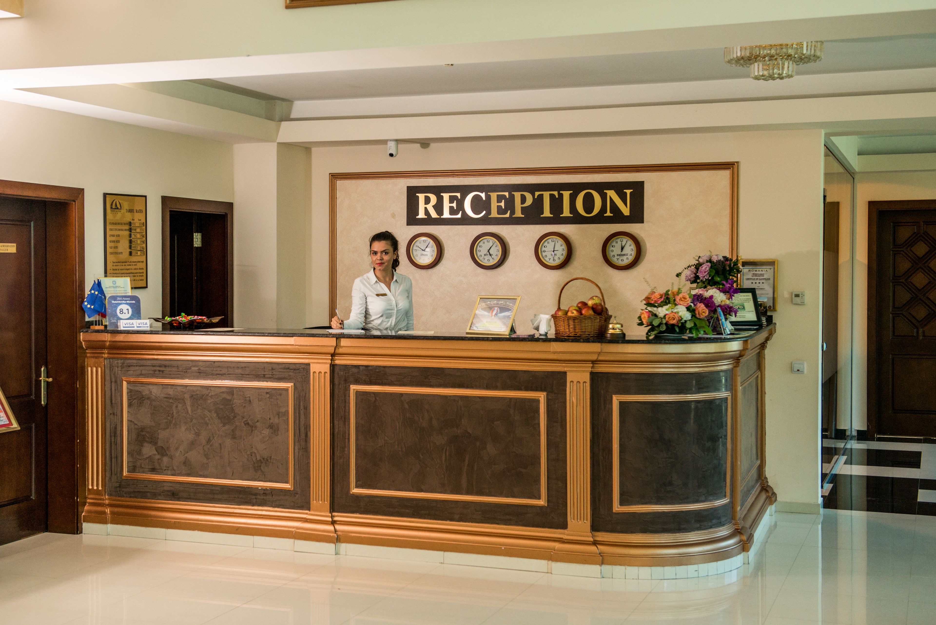 A reception desk with a sign reading "RECEPTION" above it. There are clocks on the wall, a basket, and a vase with flowers.