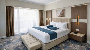 Una camera d'albergo con un letto grande, un comodino, una panca e una finestra con tende.