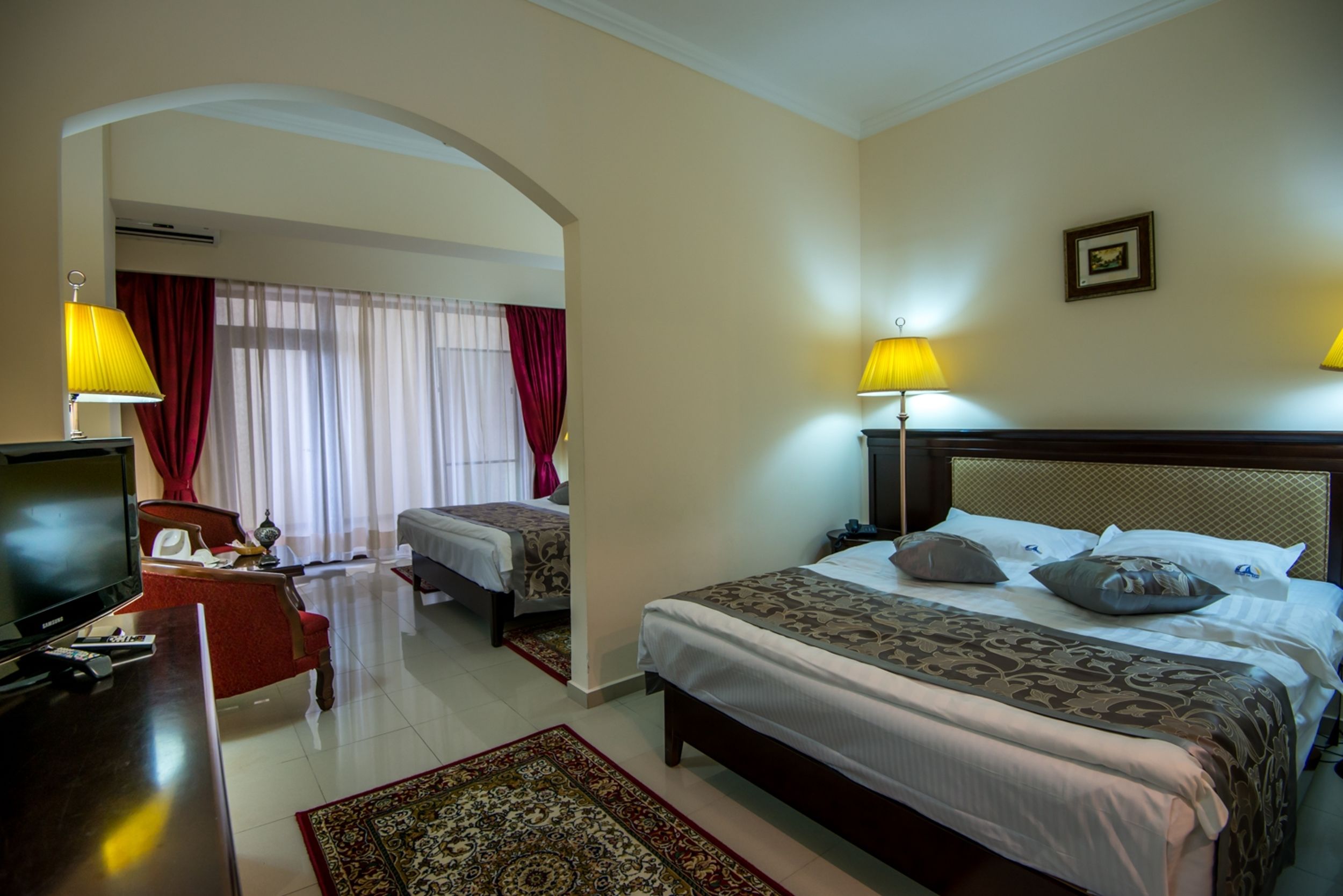 A hotel room with a large bed, a TV, a desk, and a chair. There is a window with curtains and a picture on the wall.
