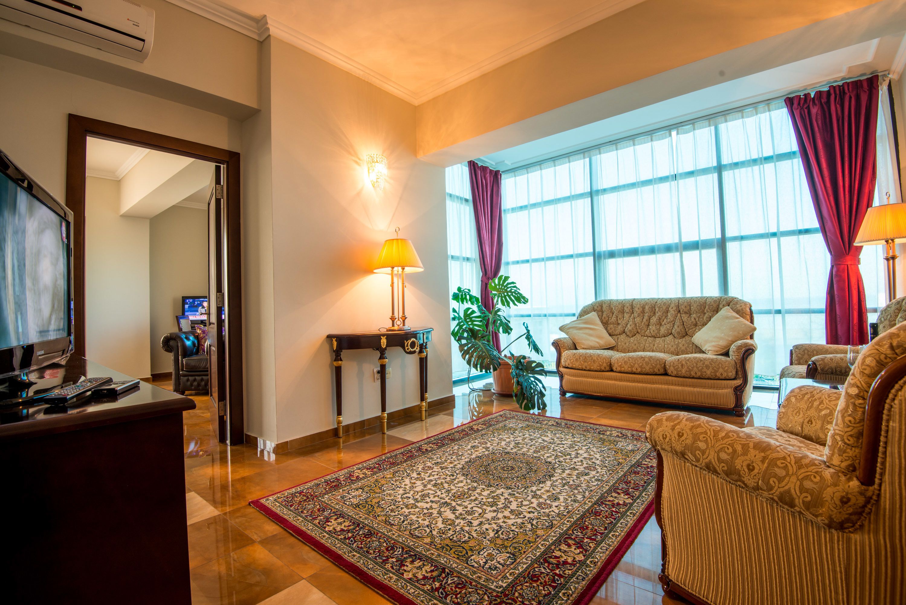A living room with a sofa, armchairs, a coffee table, a TV, and a large window with curtains.