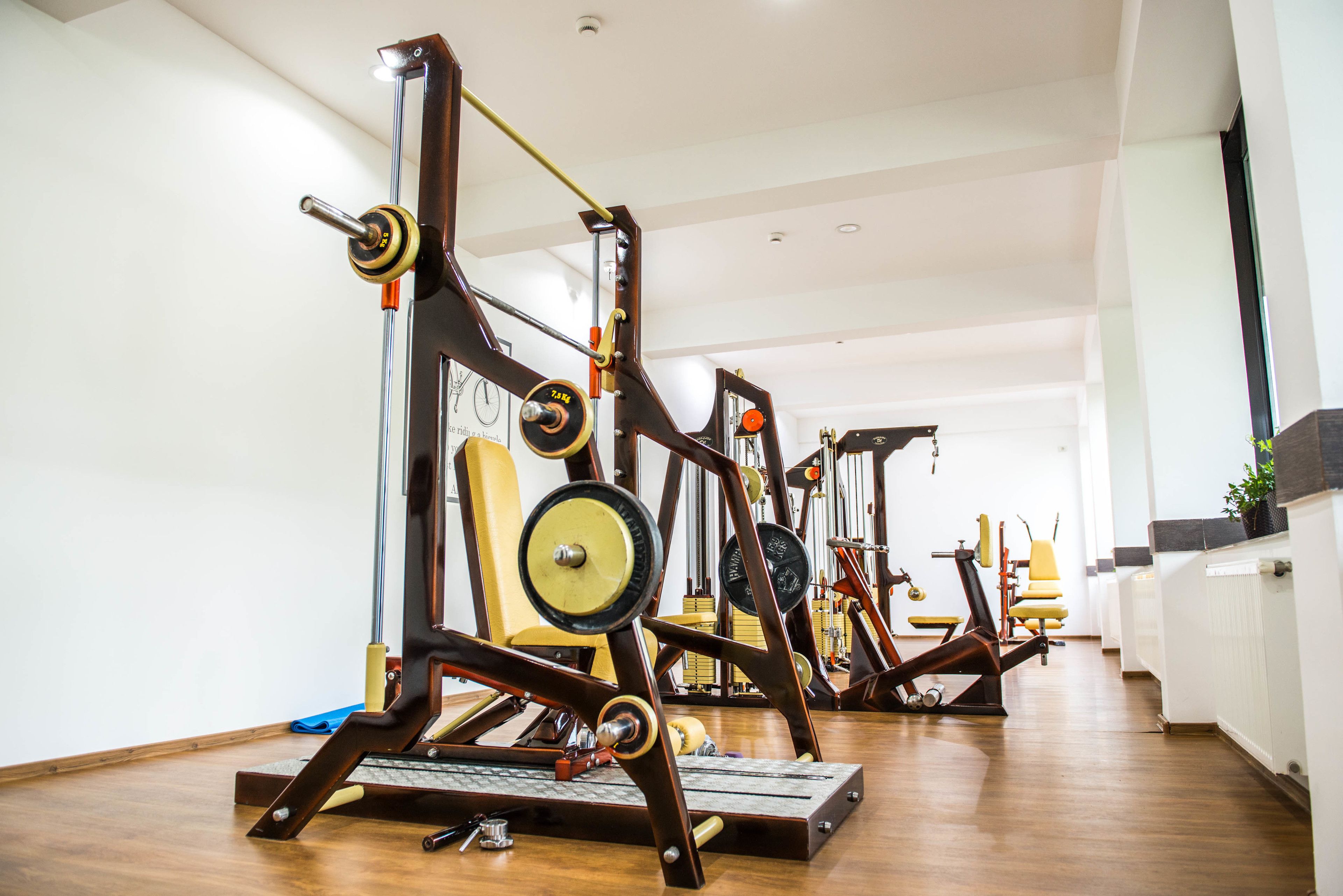 A gym with exercise equipment, wooden flooring, and a white wall.