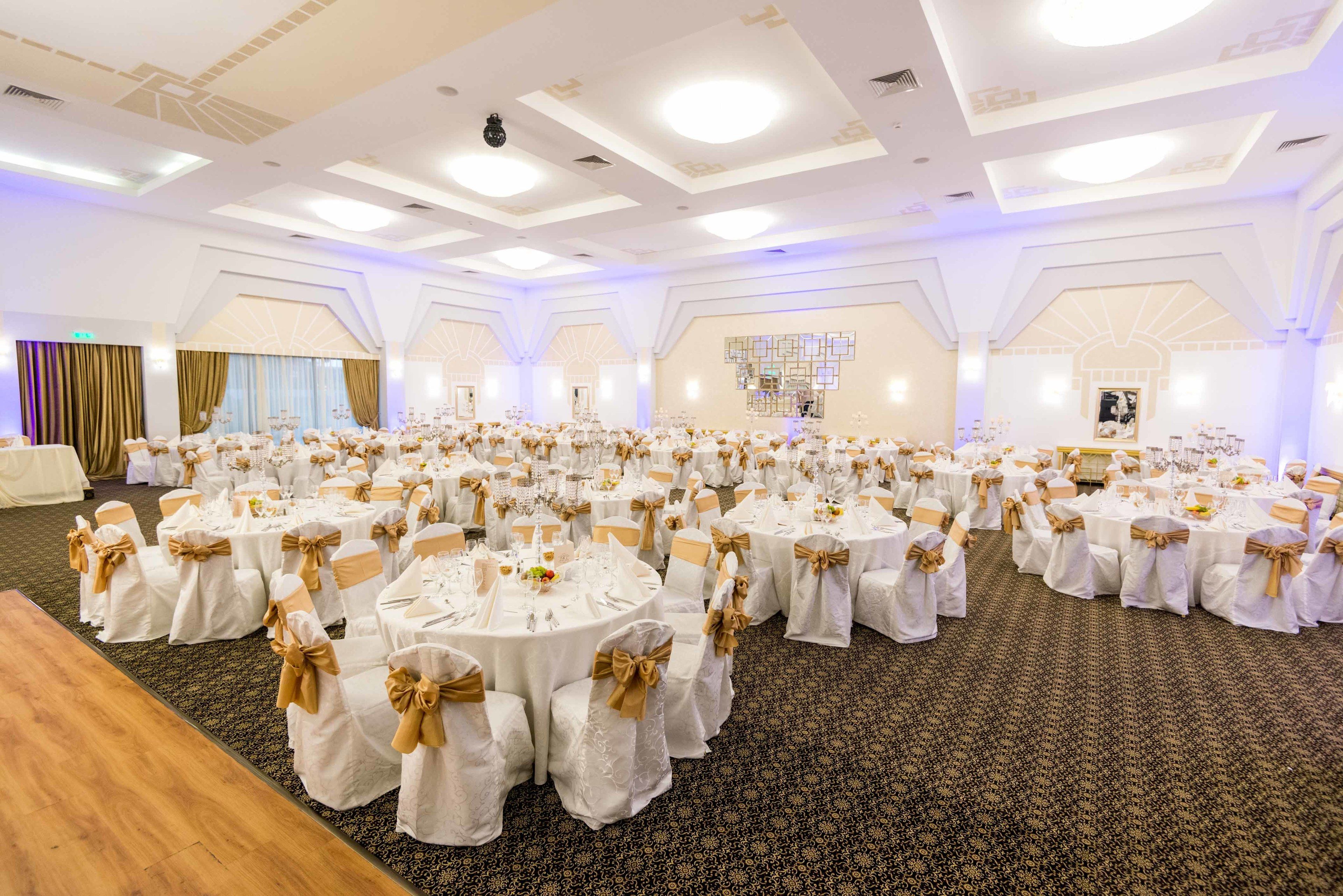 A banquet hall with round tables set for a formal event, featuring white tablecloths and gold sashes.