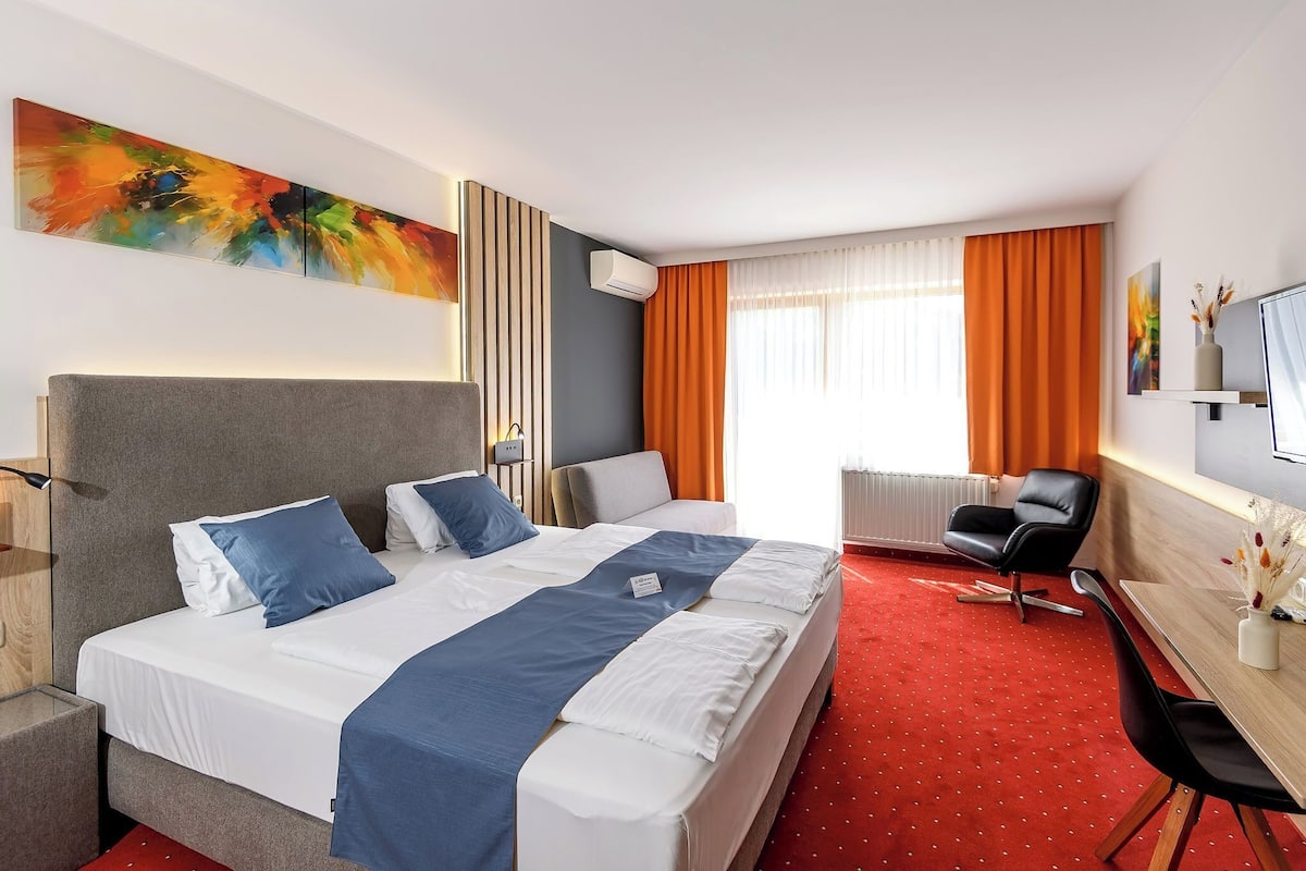 A hotel room with a large bed, a desk, a chair, and a television.