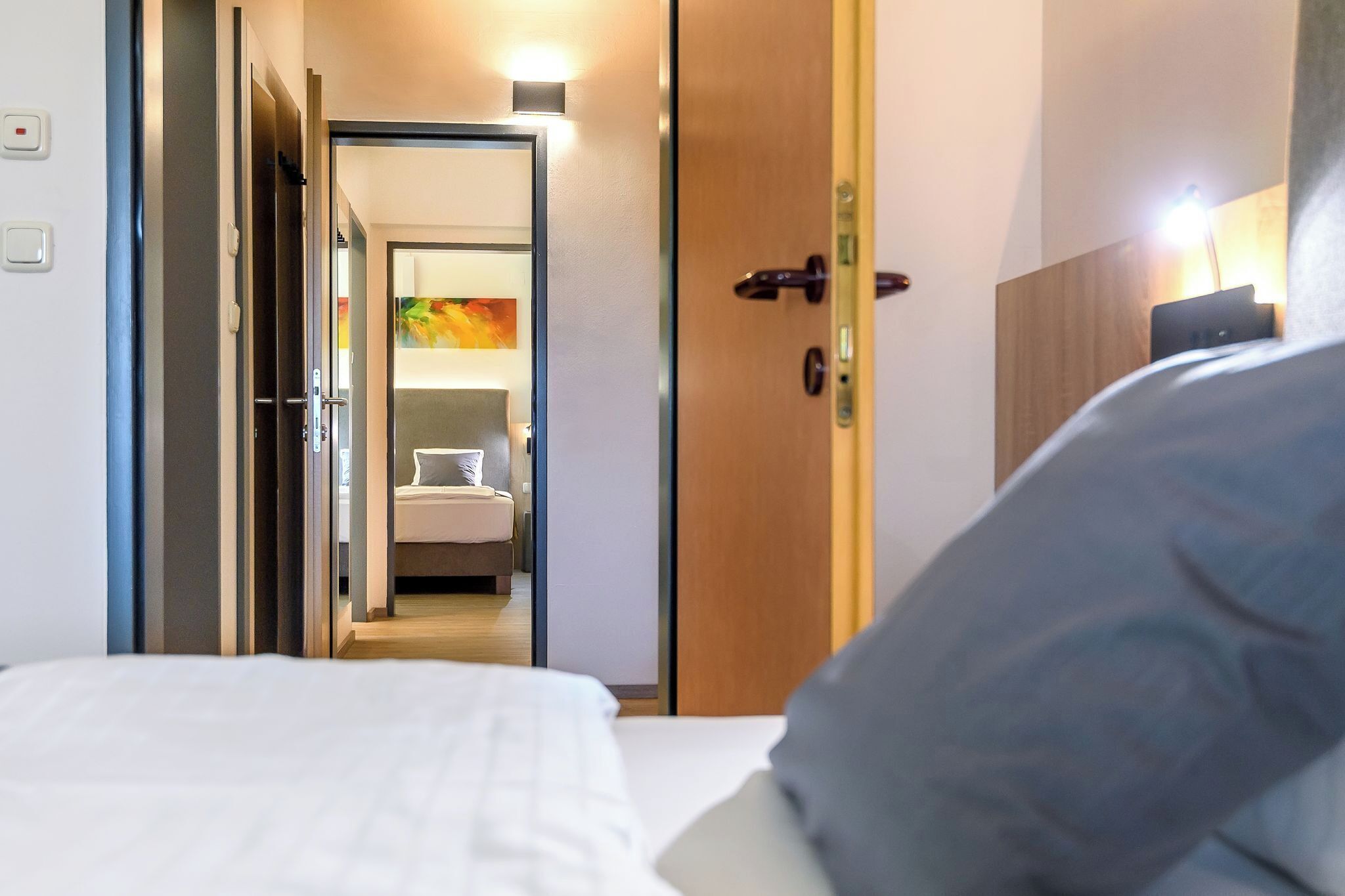 A hotel room with a bed, a door leading to a bathroom, and a small desk with a lamp.