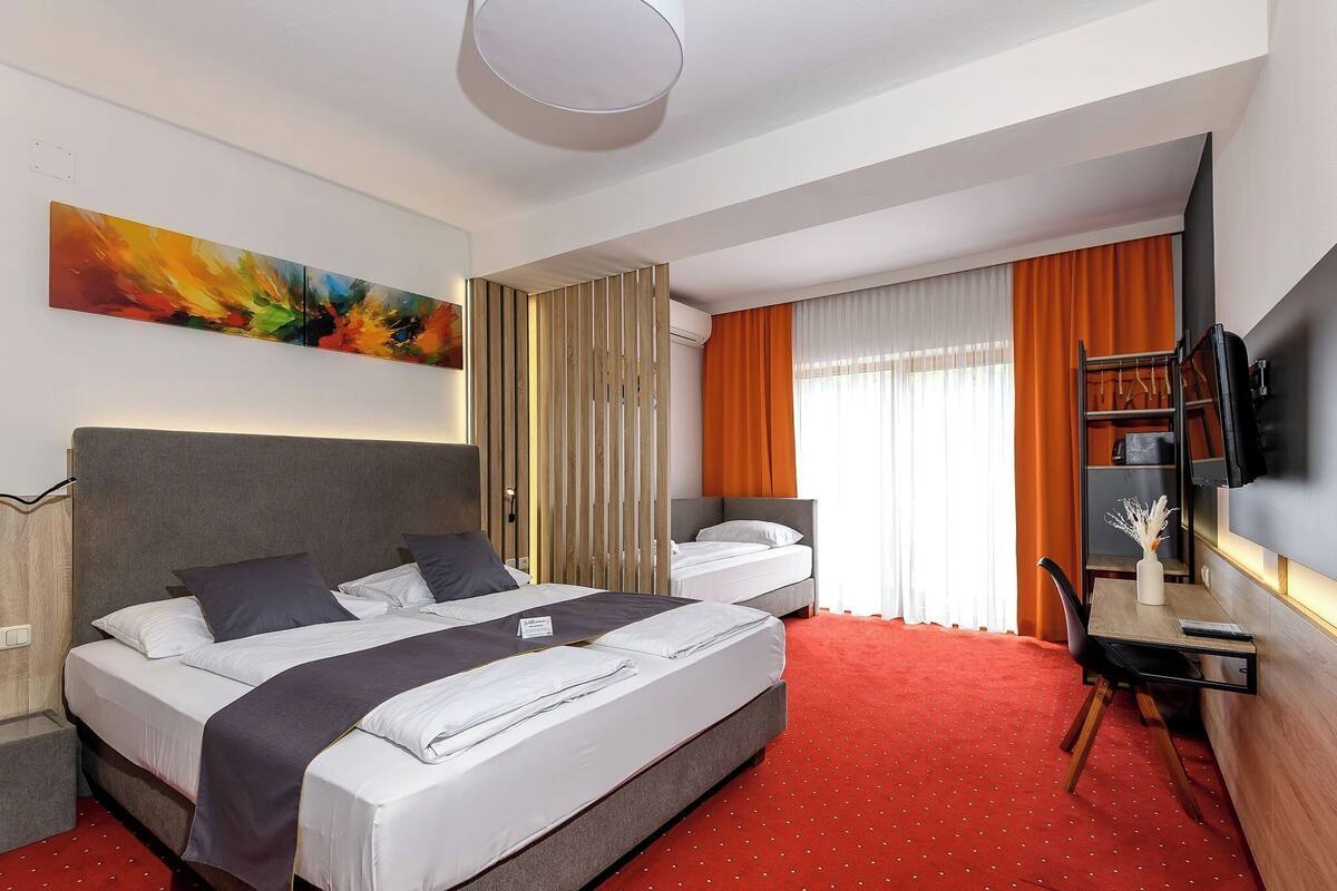 A hotel room with two beds, a desk, a chair, a TV, and a large abstract painting on the wall.