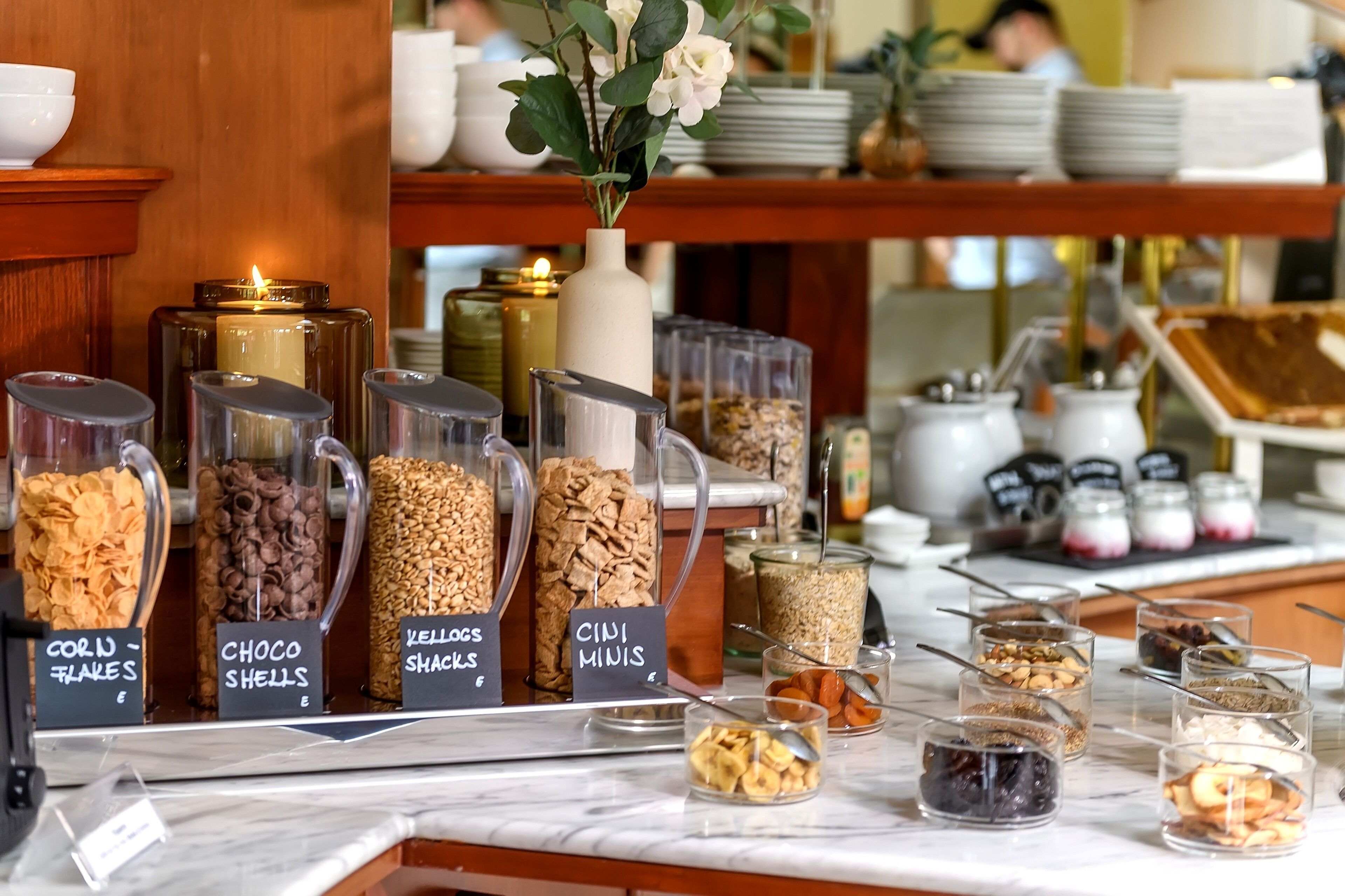 Un buffet de petit-déjeuner avec des récipients étiquetés contenant des céréales, des noix et des fruits secs.