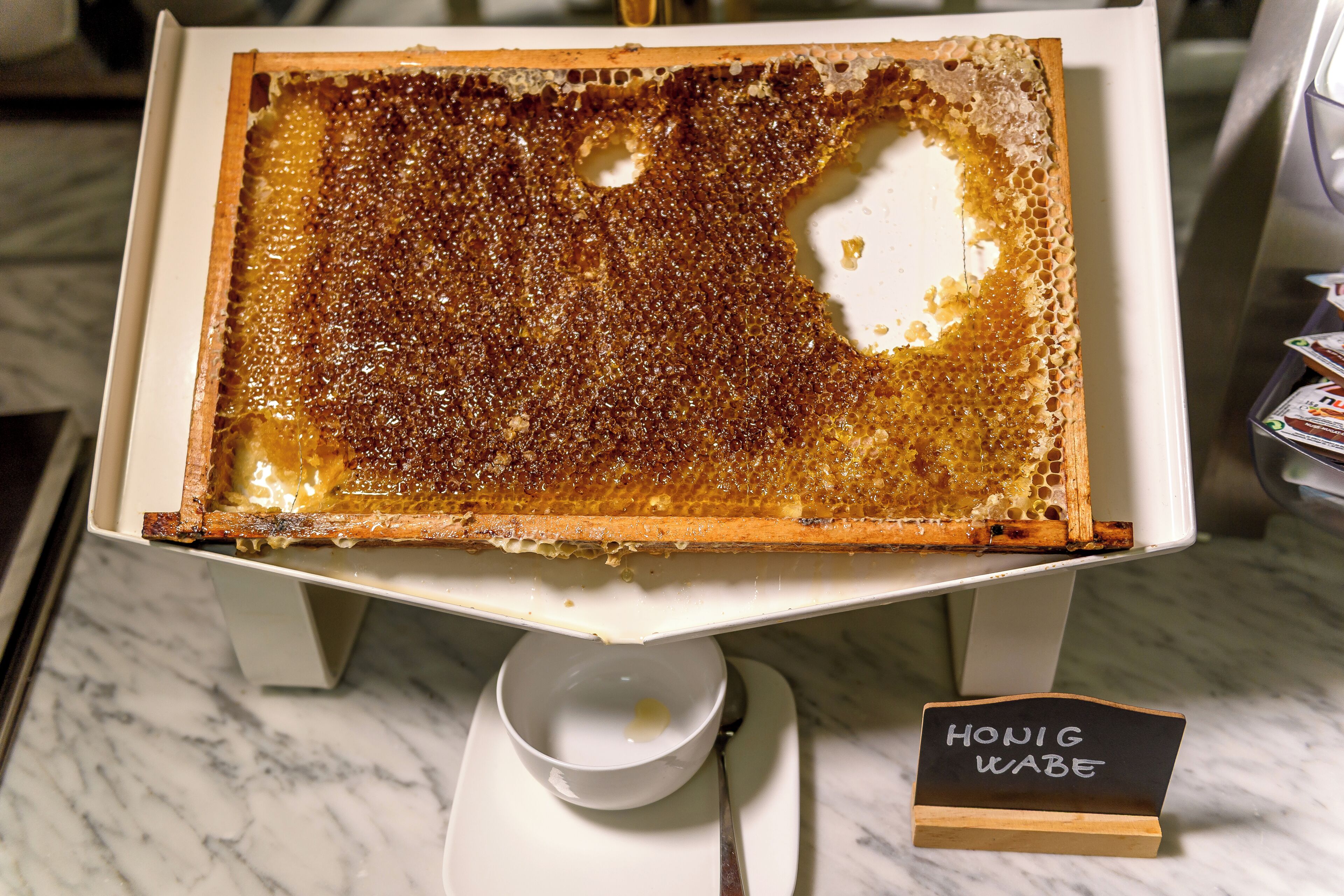 A honeycomb dessert on a white stand with a sign reading 'Honey Wabe'.