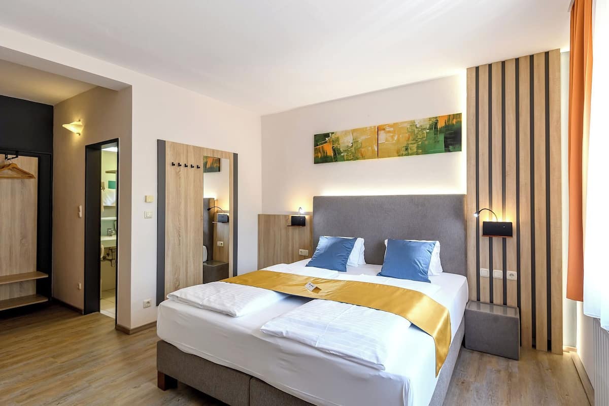 A modern hotel room with a large bed, a wardrobe, a mirror, and a wall-mounted artwork.