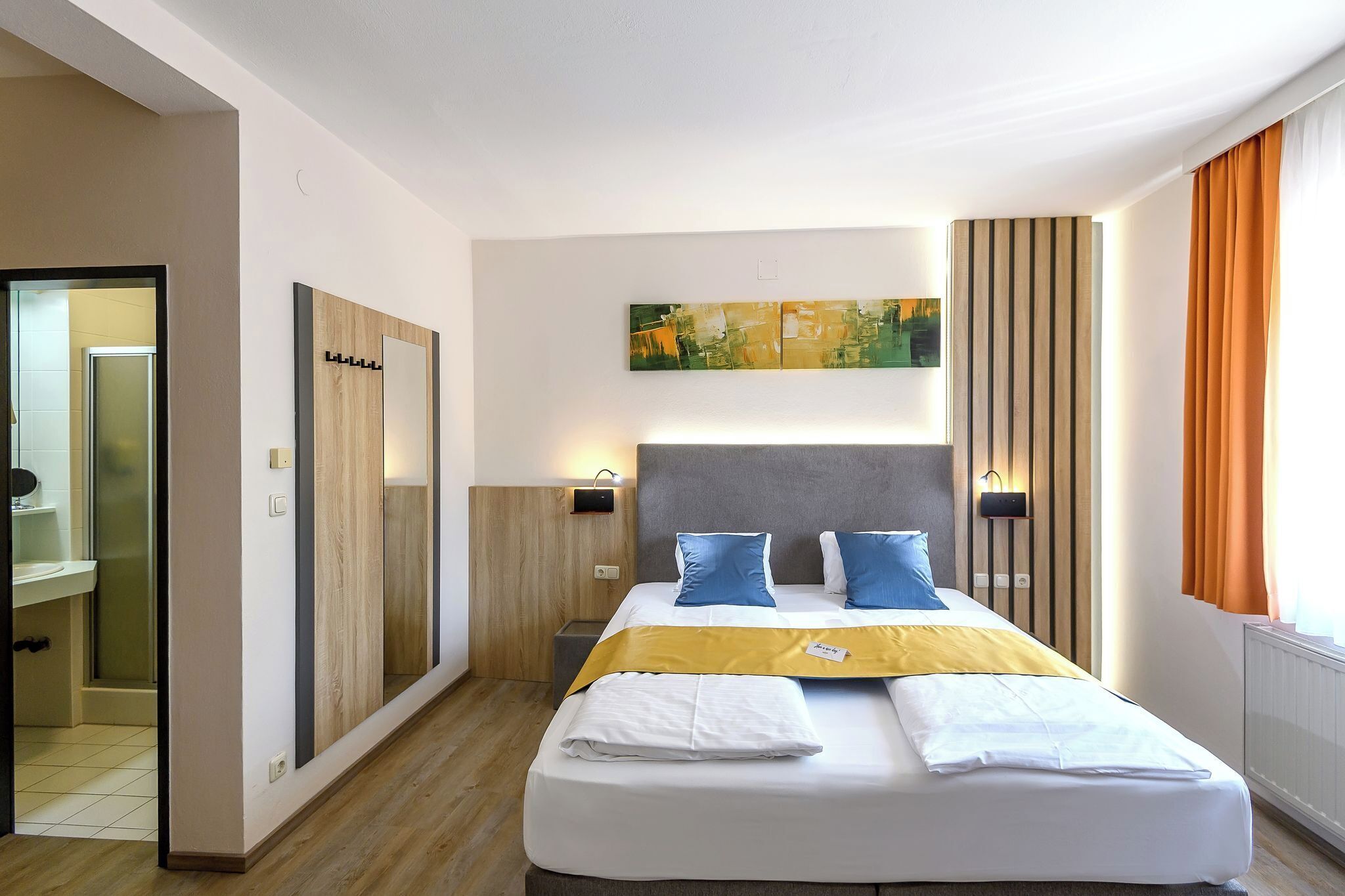A hotel room with a bed, a painting, a wardrobe, and a window with curtains.