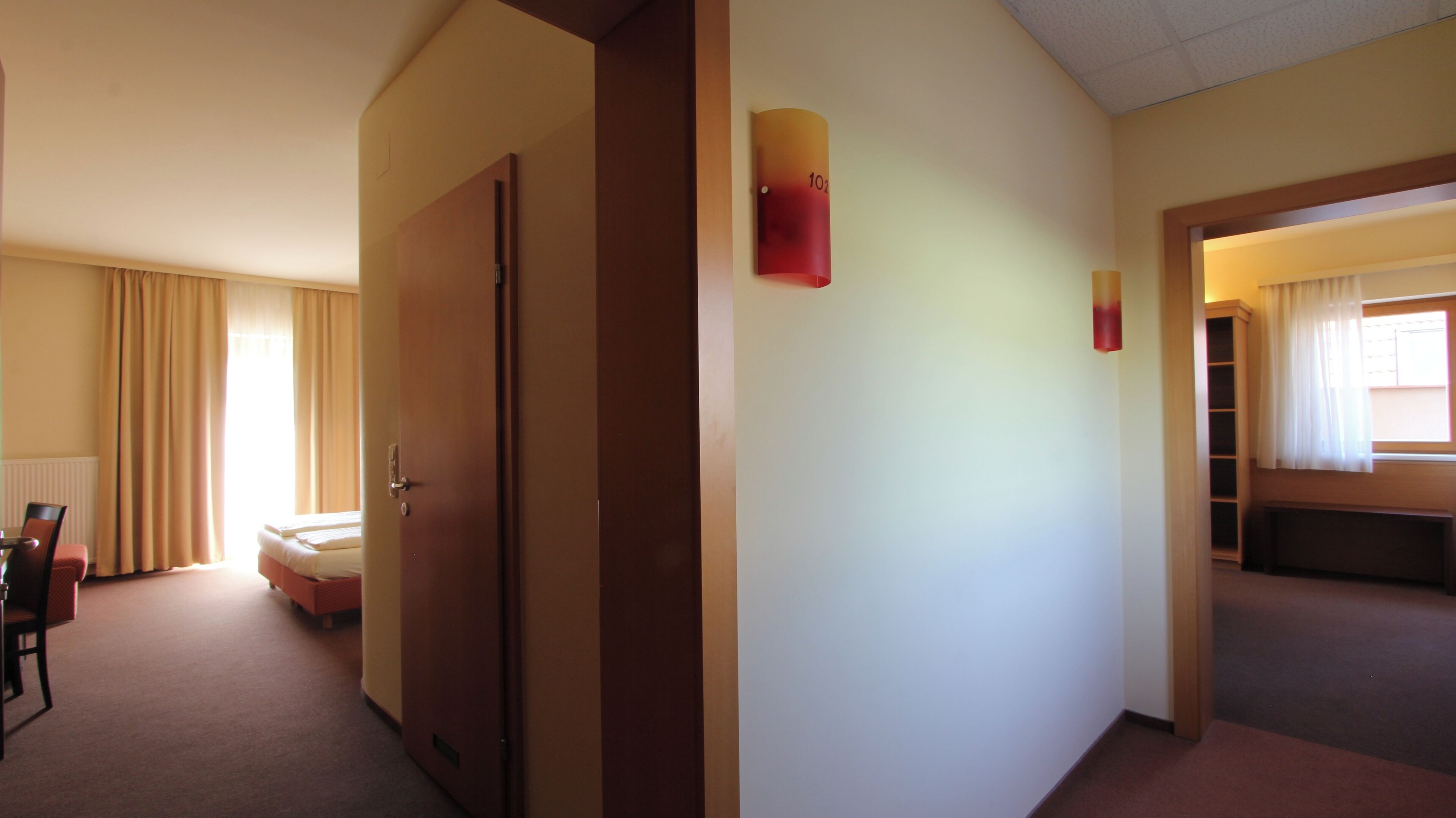 A hotel hallway with a bed, a desk, and a chair.