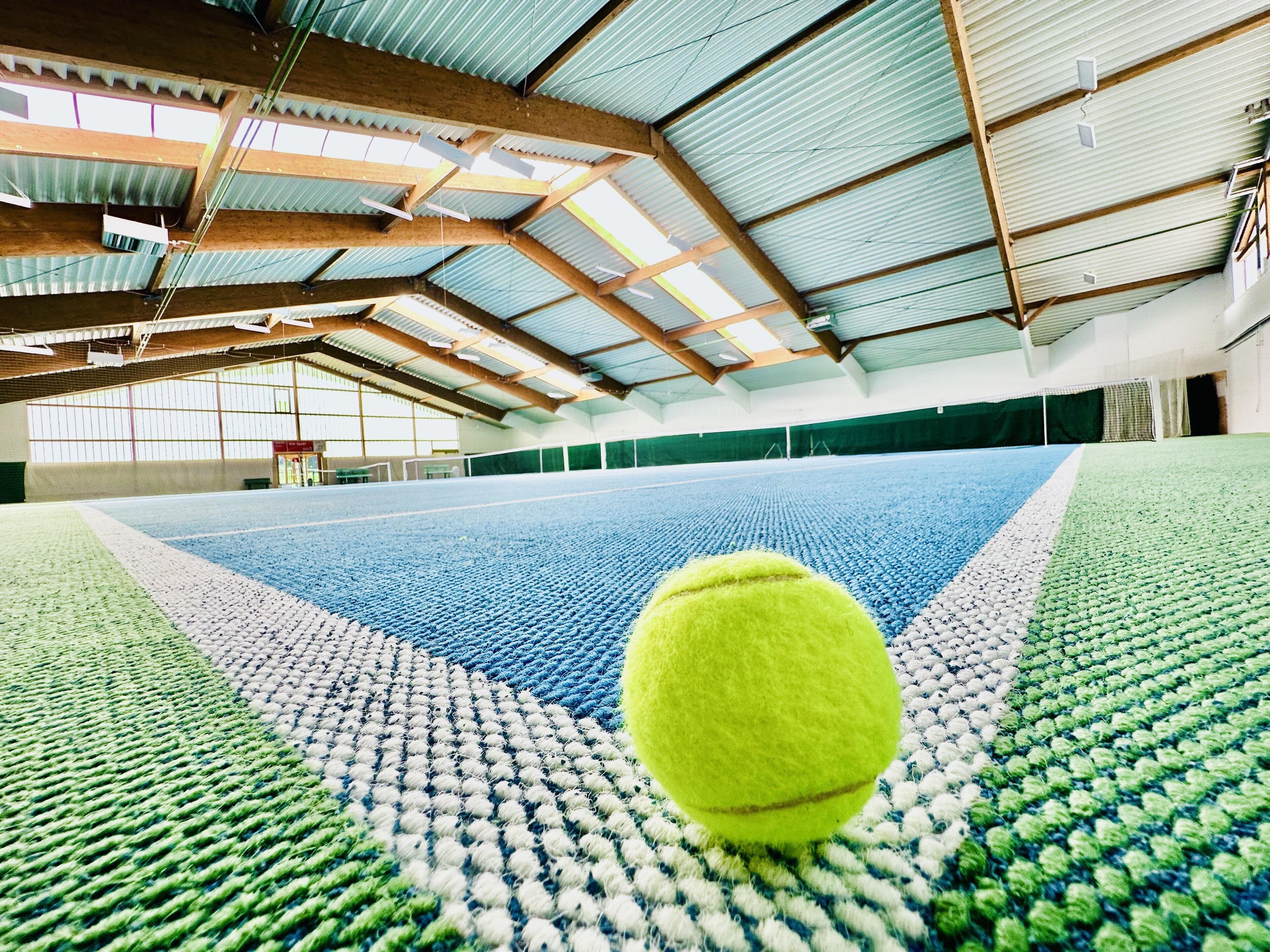 Cancha de tenis interior con una pelota de tenis en primer plano.