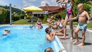 A swimming pool area with people, a building with a red roof, and a yellow umbrella. - Vital Hotel Krainz mit Nebenhaus Familien Hotel (Jennersdorf)