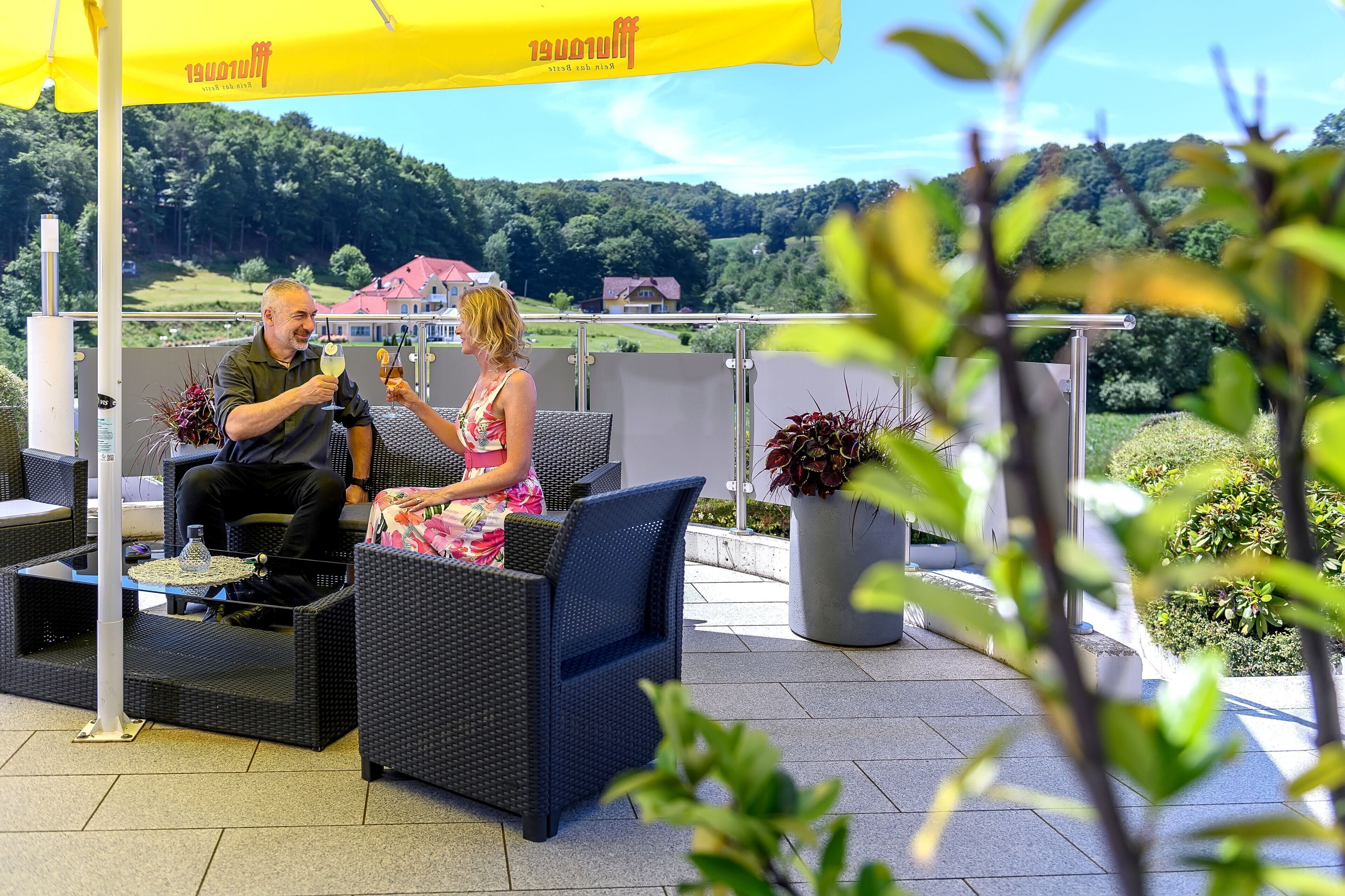 Una terraza con mobiliario de mimbre, una sombrilla amarilla y vistas a un paisaje verde.