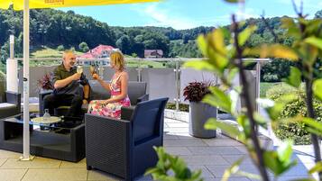 A terrace with wicker furniture, a yellow umbrella, and a view of a green landscape.