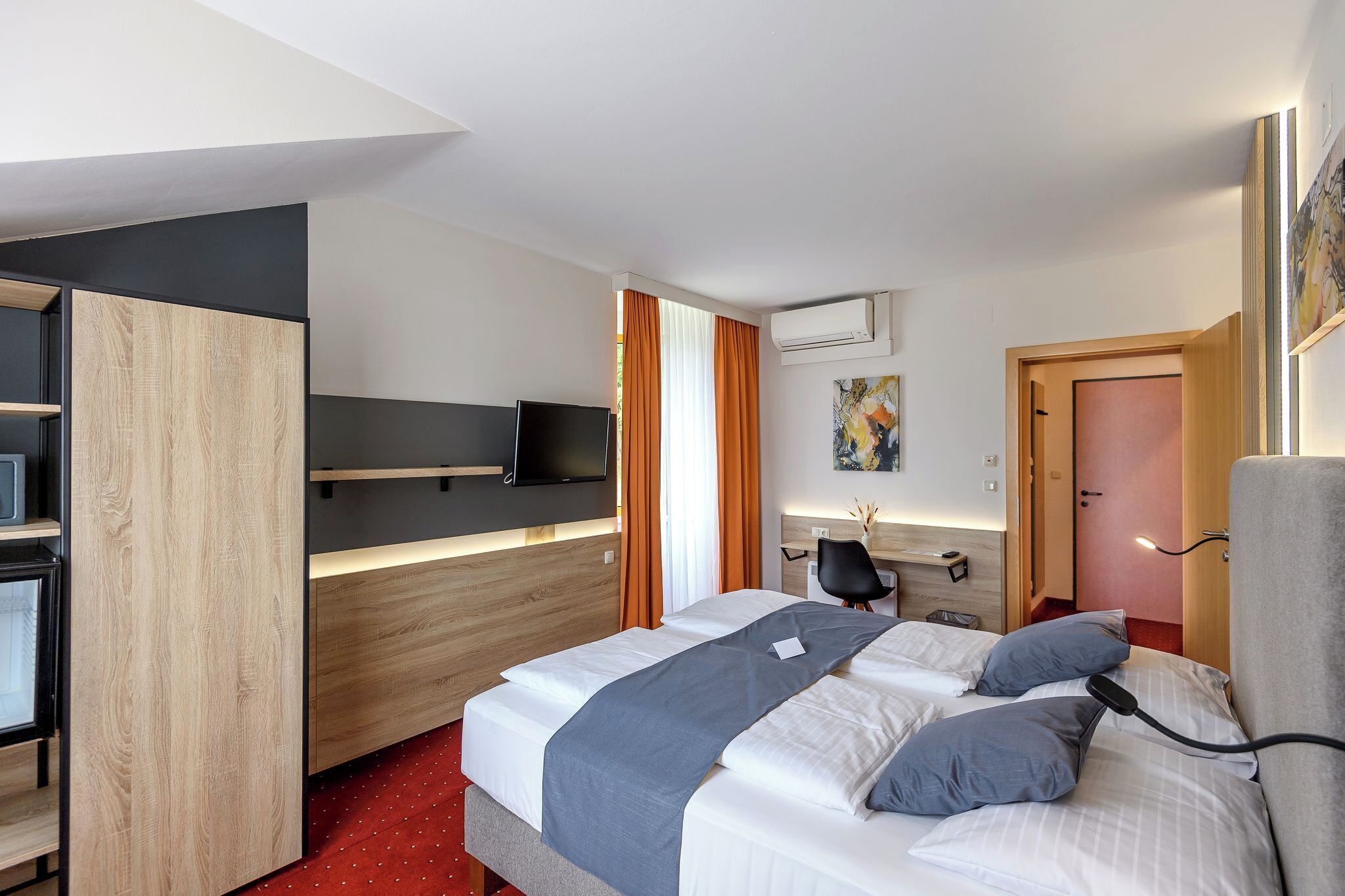 Una camera d'albergo con un letto, una scrivania con una sedia, una televisione e un condizionatore d'aria.