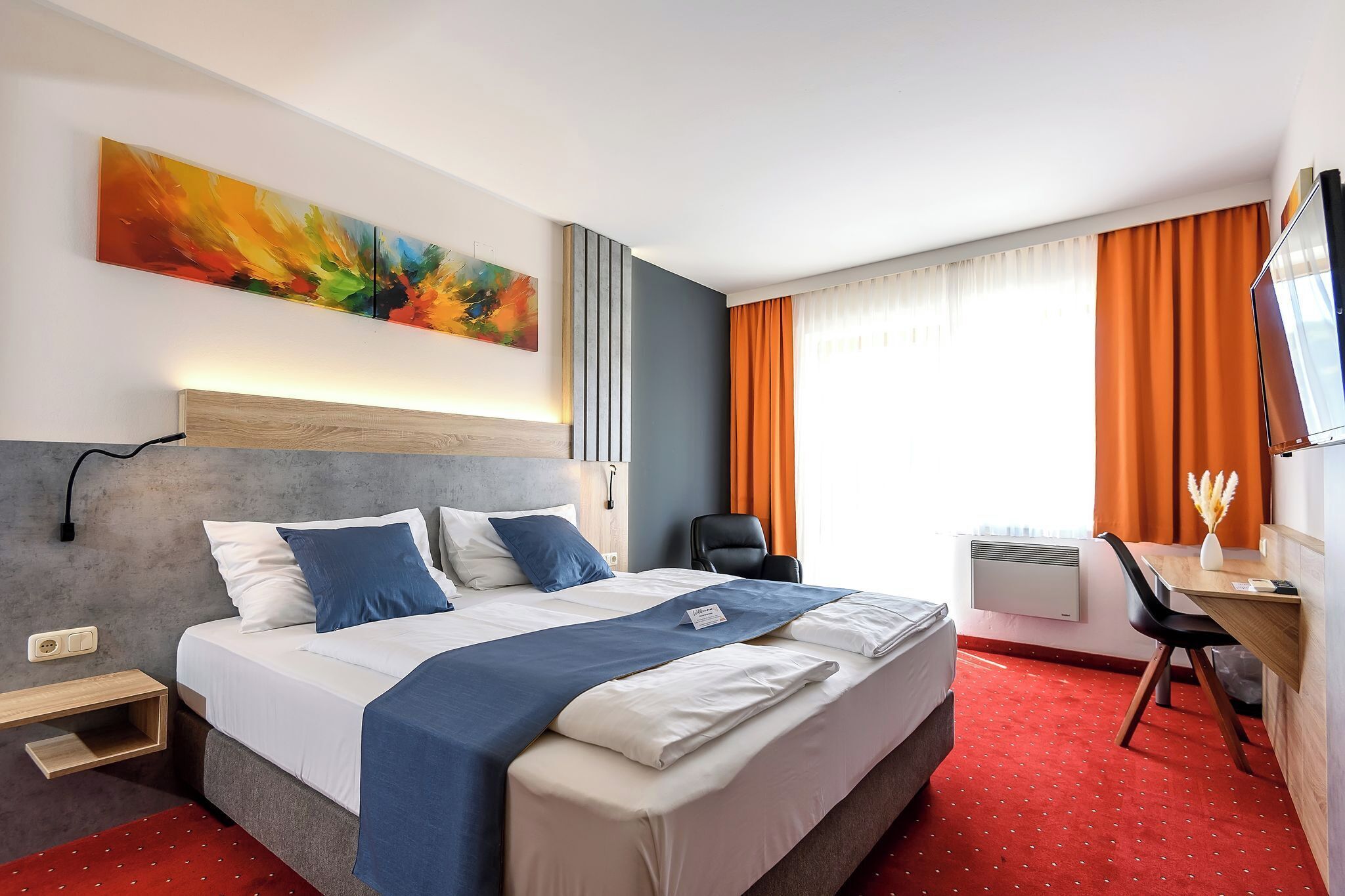 A hotel room with a large bed, a desk with a chair, a TV, and a window with curtains.