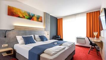 A hotel room with a large bed, a desk with a chair, a TV, and a window with curtains.