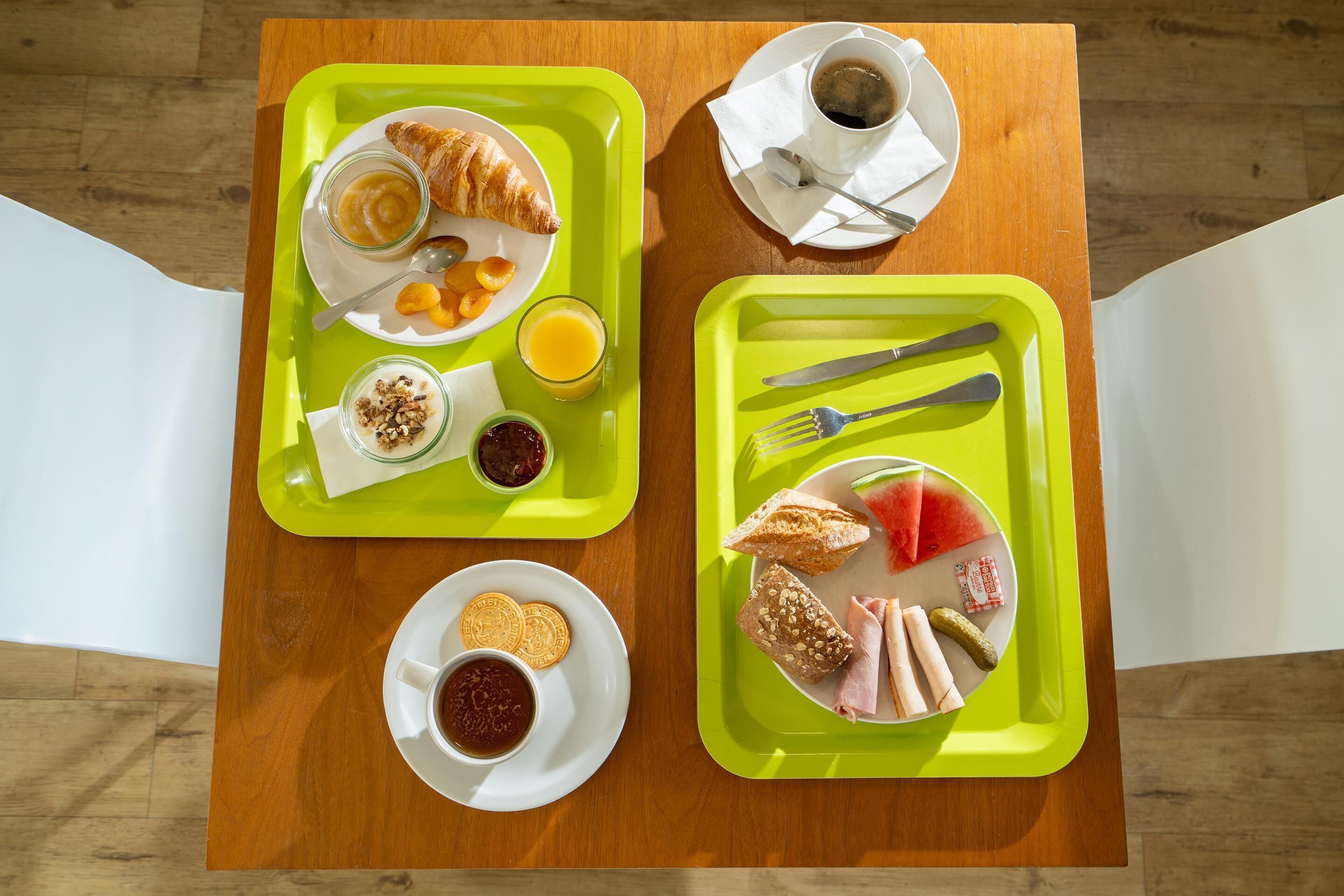 Aamiaistarjotin, jossa on croissantteja, appelsiinimehua, jogurttia ja leipää, puisella pöydällä.