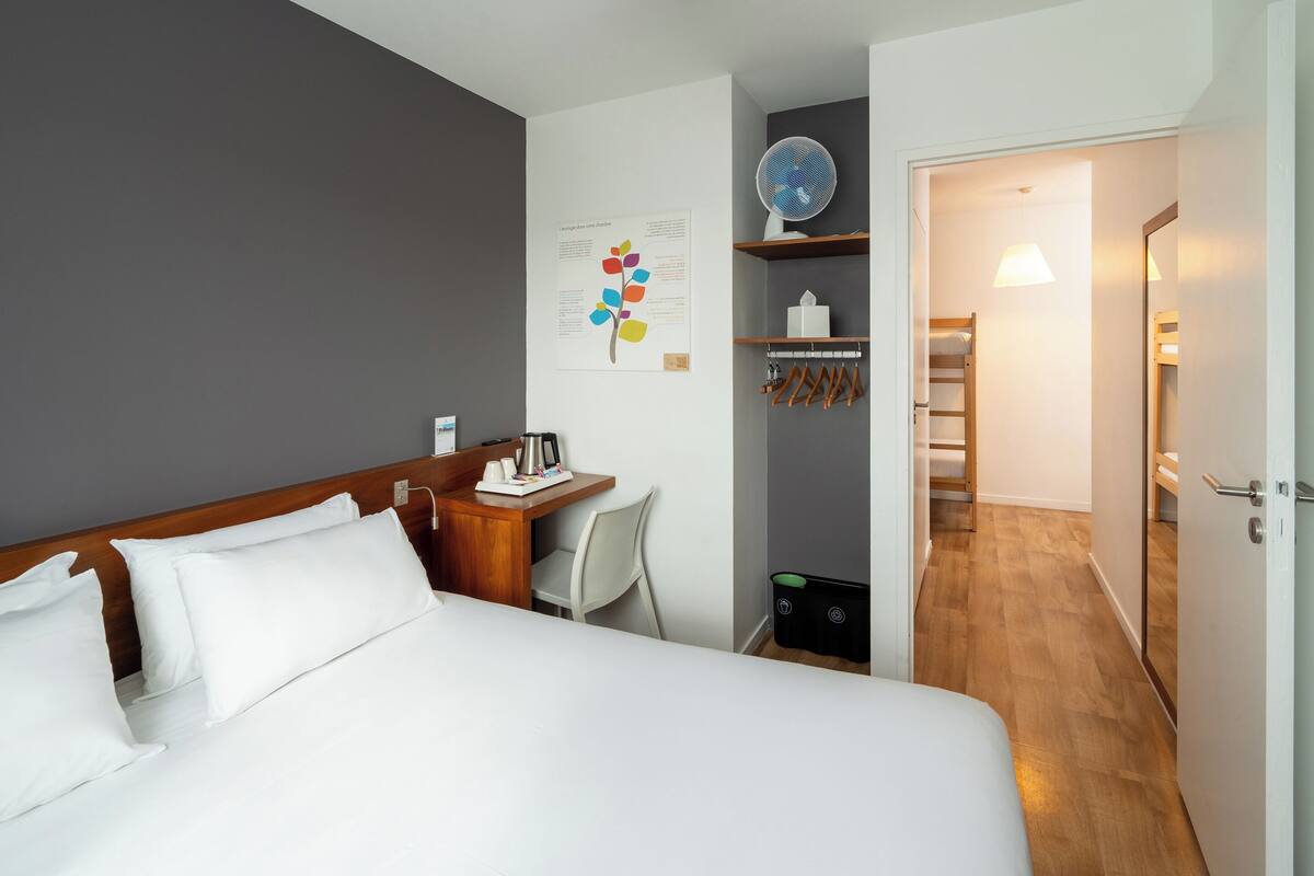 Une chambre d’hôtel avec un lit, un bureau, une chaise, un globe terrestre et un mur orné d ’une affiche.