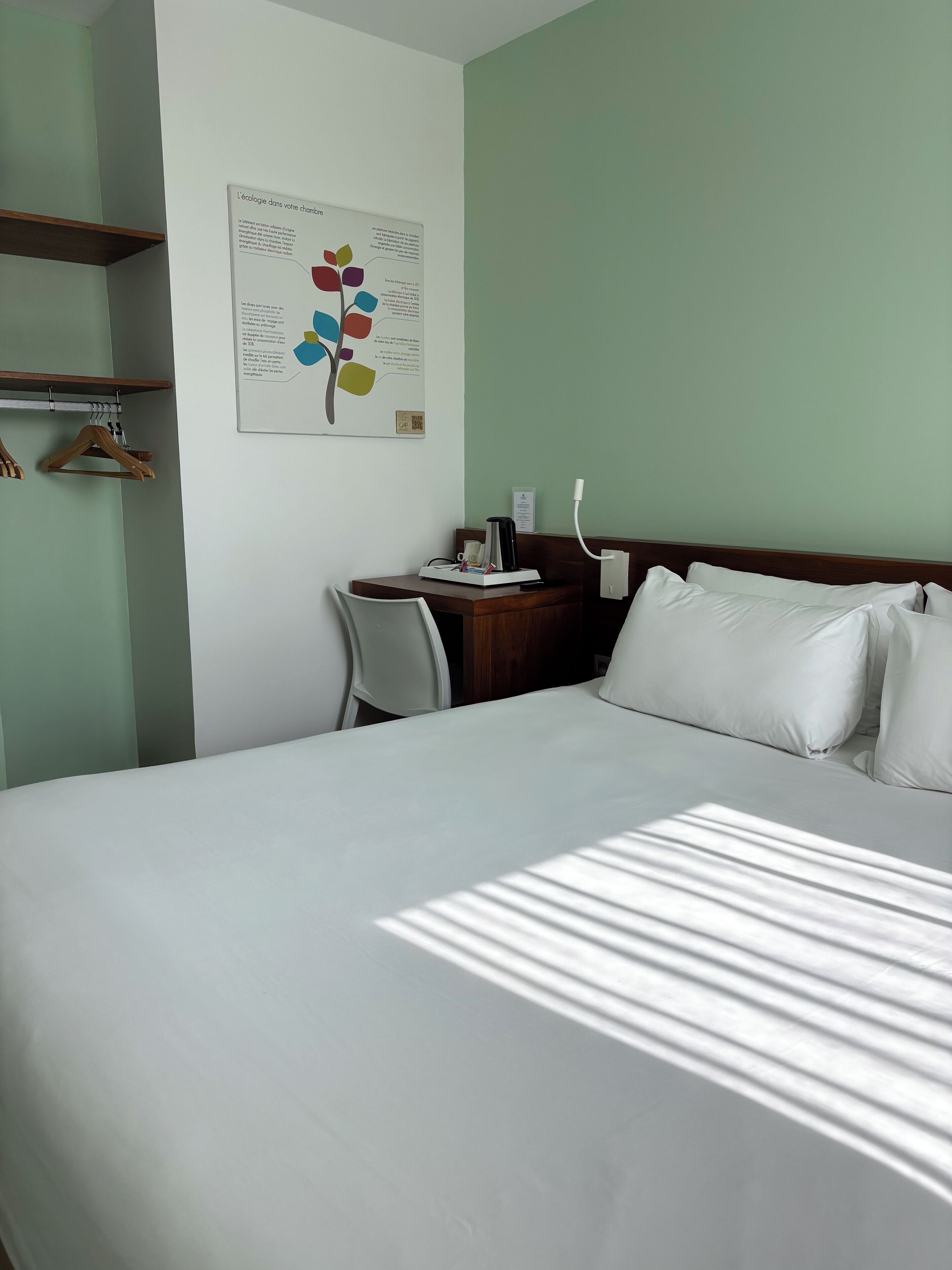 Ett hotellrum med en säng, ett skrivbord och en stol. På väggen sitter en skylt med text och en färgstark design.