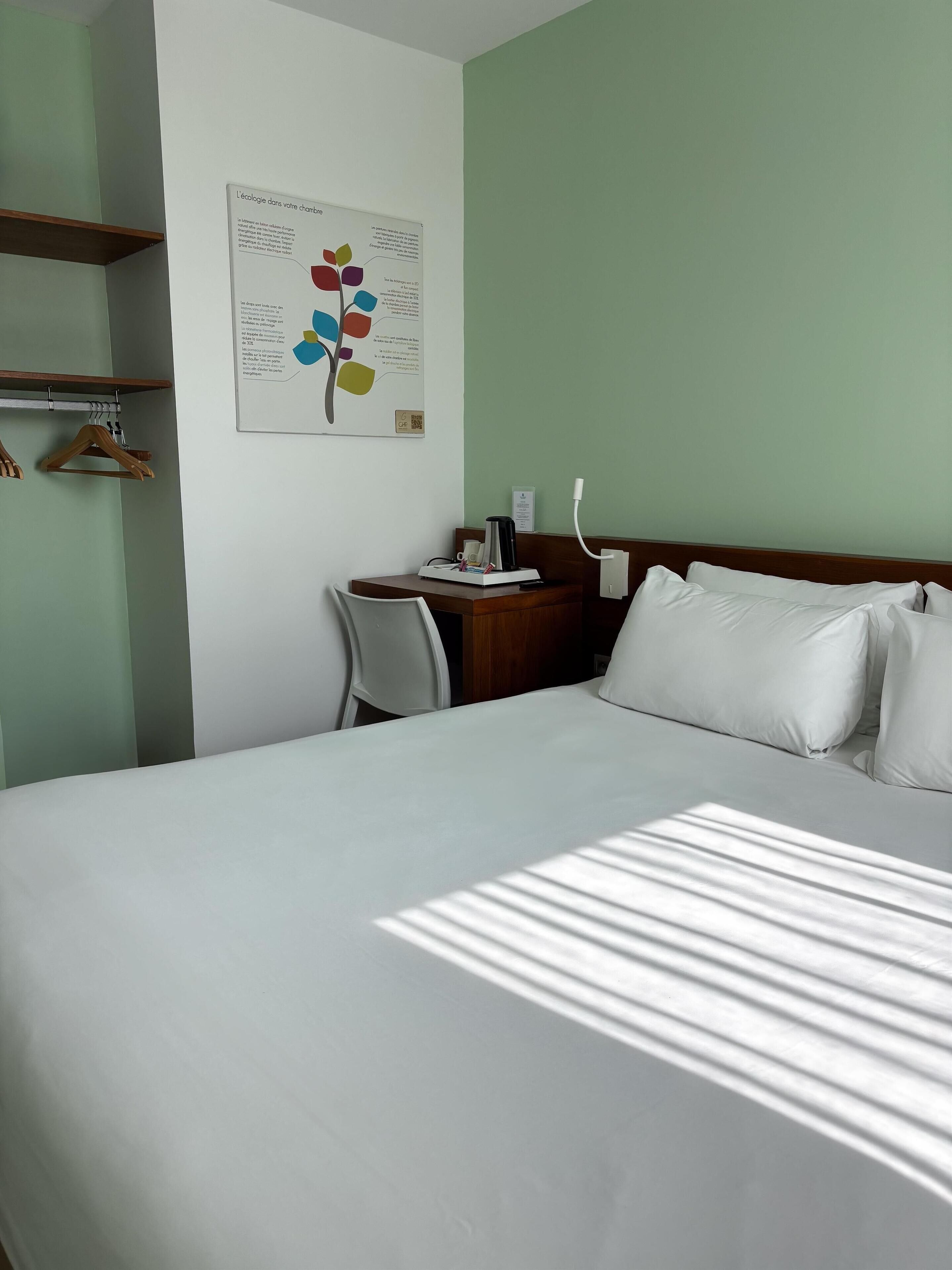 A hotel room with a bed, a desk, and a wall-mounted poster.