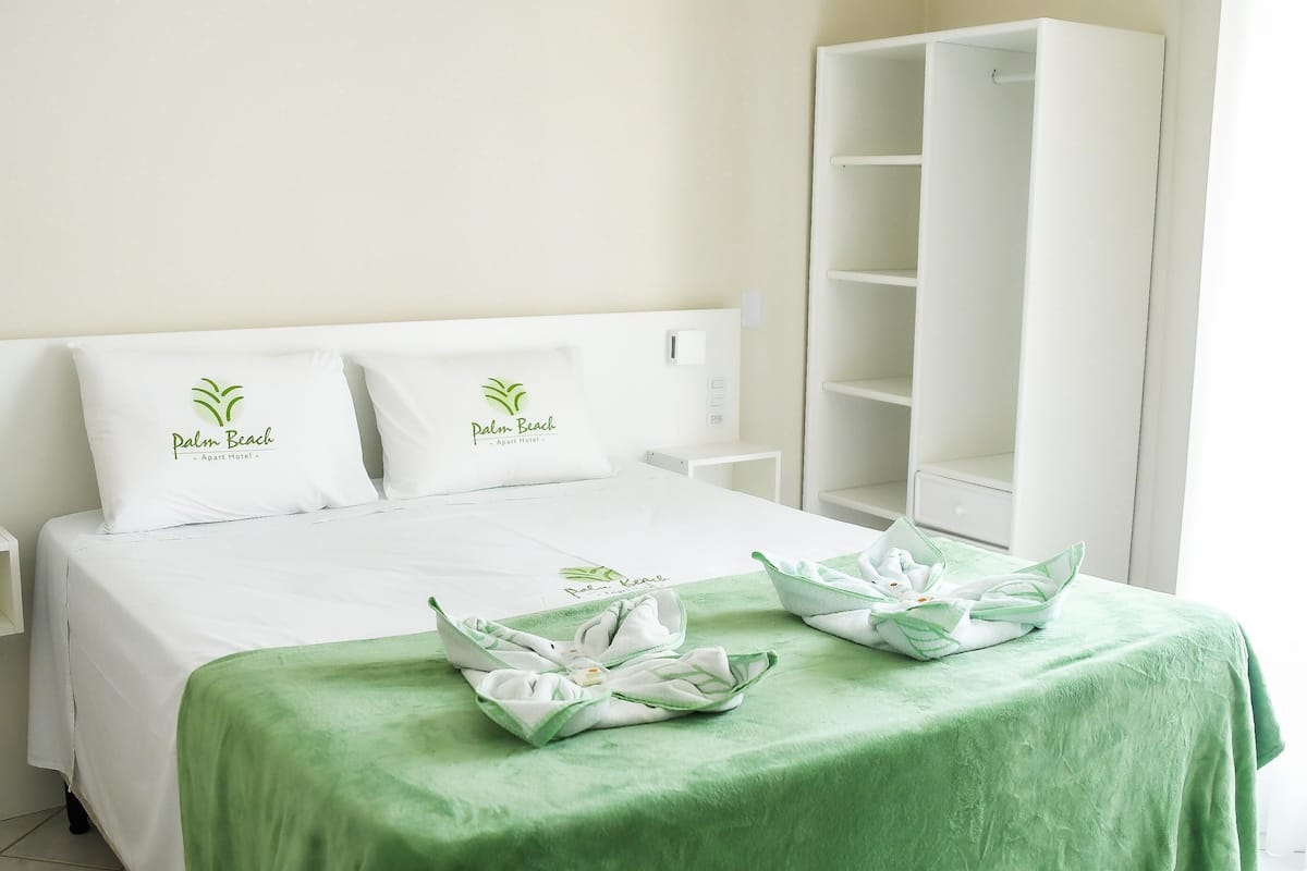 A hotel room with a bed, two pillows, a green bedspread, and a white wardrobe.
