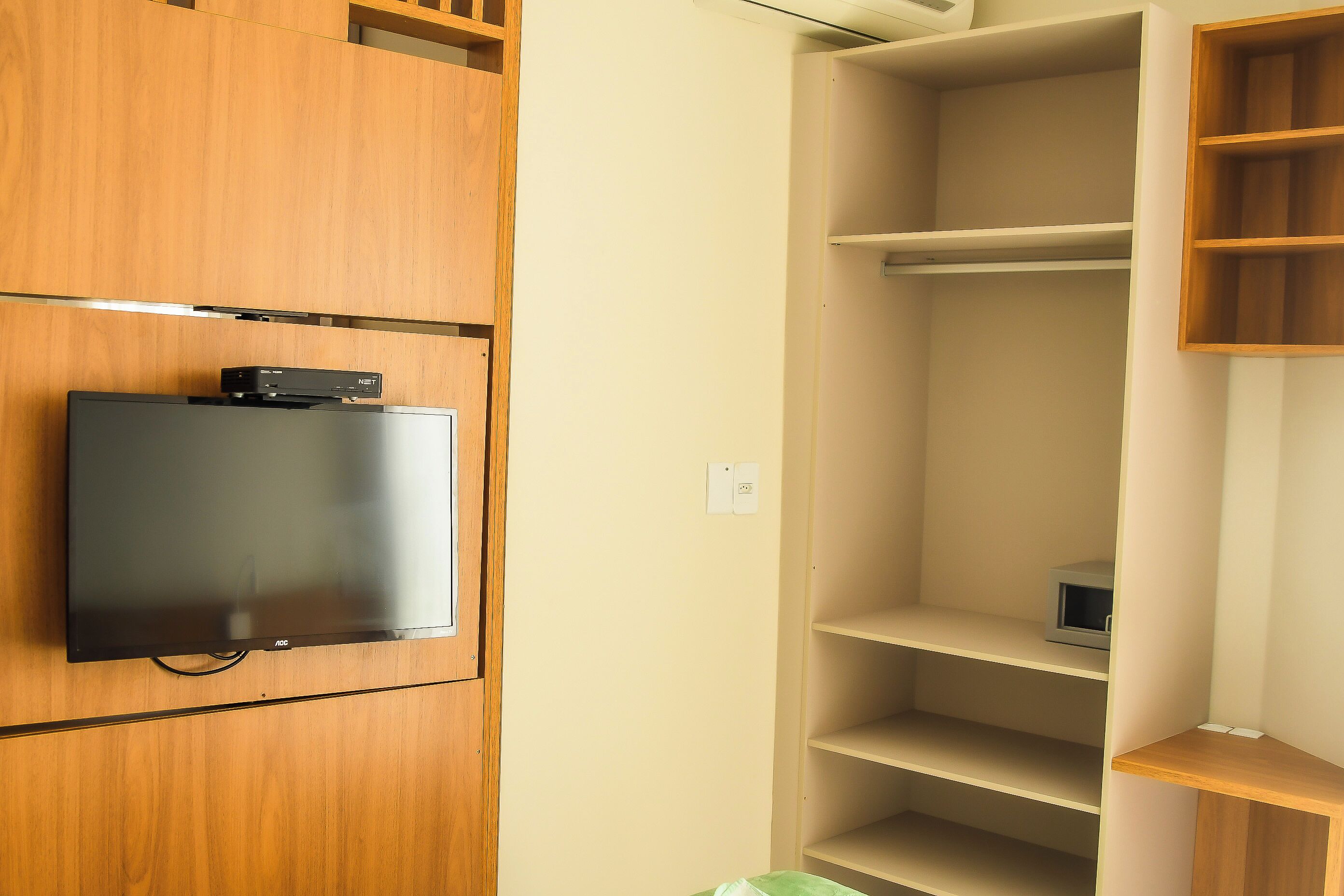 Quarto com televisão de tela plana fixada em um móvel de madeira, estante embutida e tomada na parede.