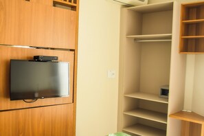 A room with a flat-screen TV mounted on a wooden cabinet, a built-in shelf unit, and a power outlet on the wall. - Palm Beach Apart Hotel (Florianópolis)